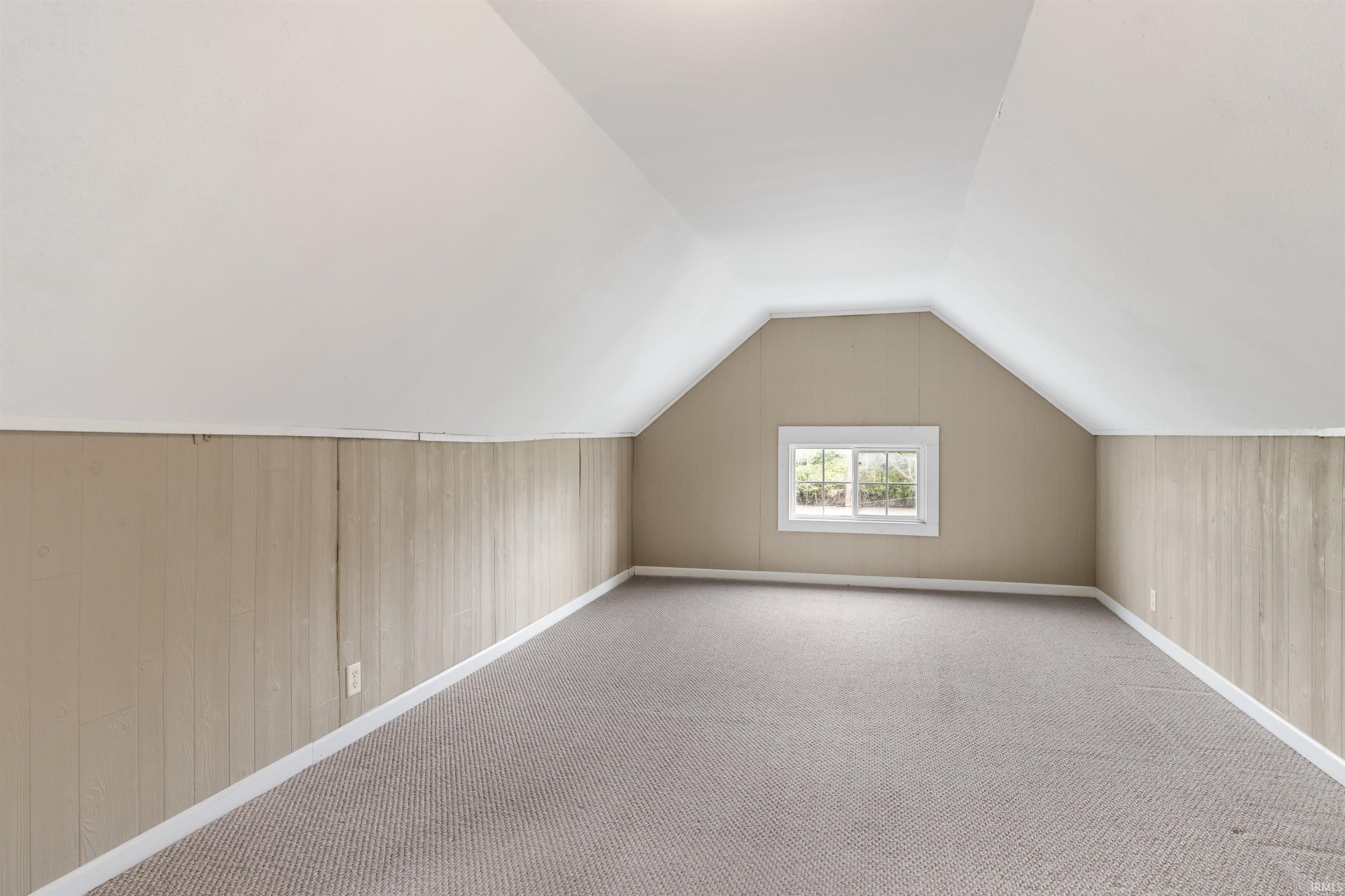 Carpeted room featuring sloped ceilings, paneling, and a white-framed window