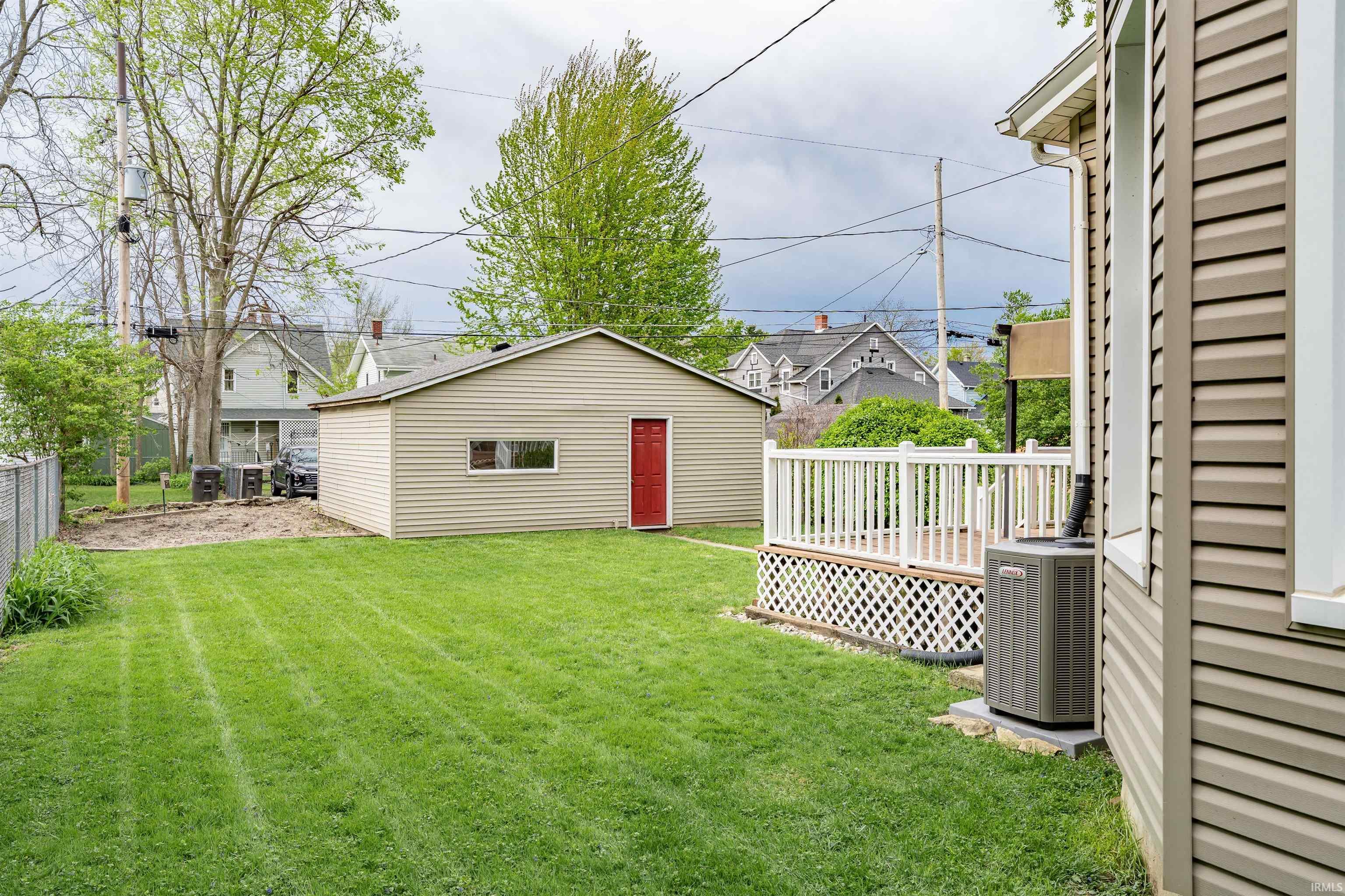 Spacious backyard featuring a detached garage with a red door, a deck with white railings, and a chain-link fence
