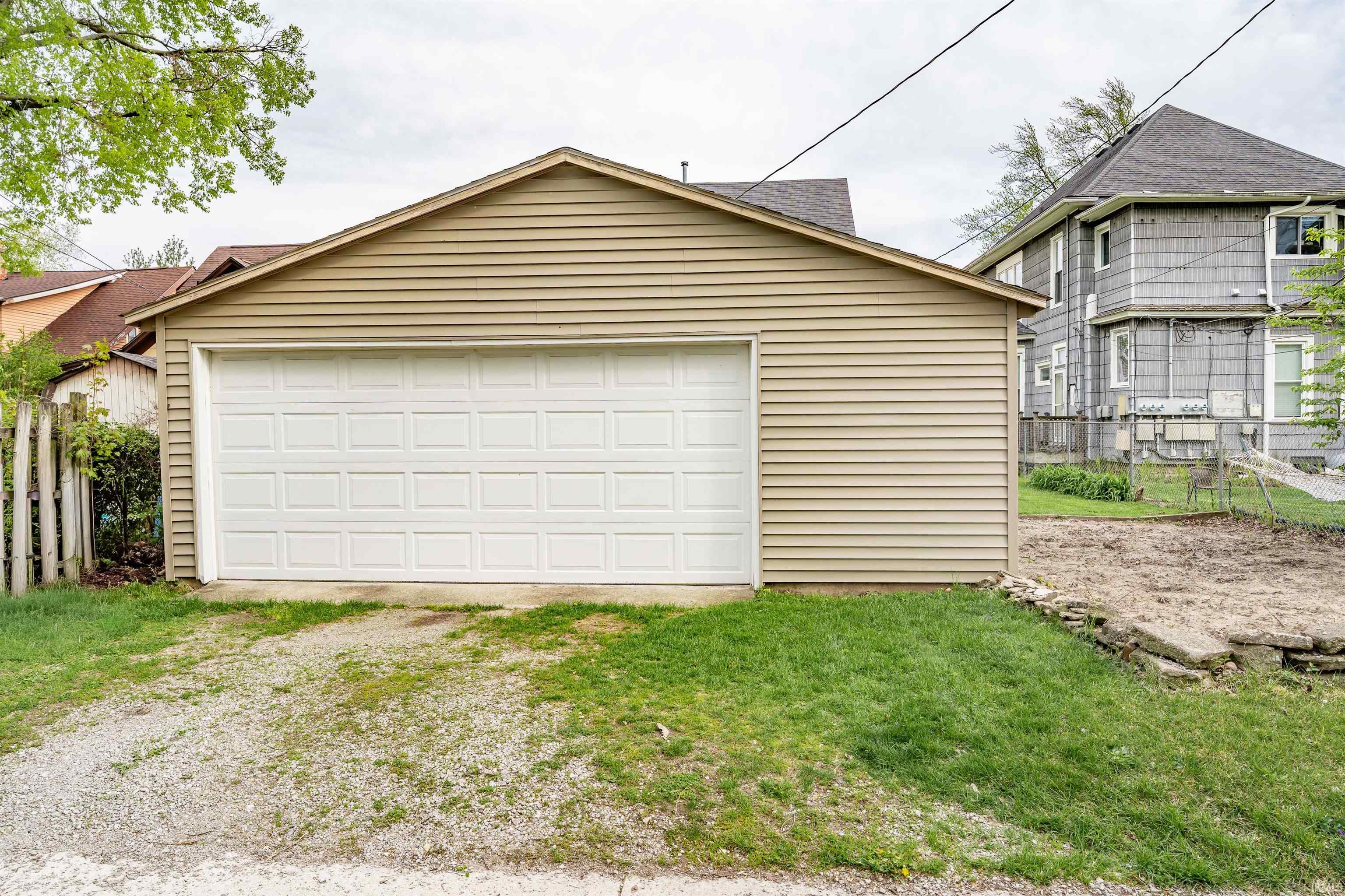Detached garage with horizontal siding, a white paneled garage door, and a gravel driveway apron