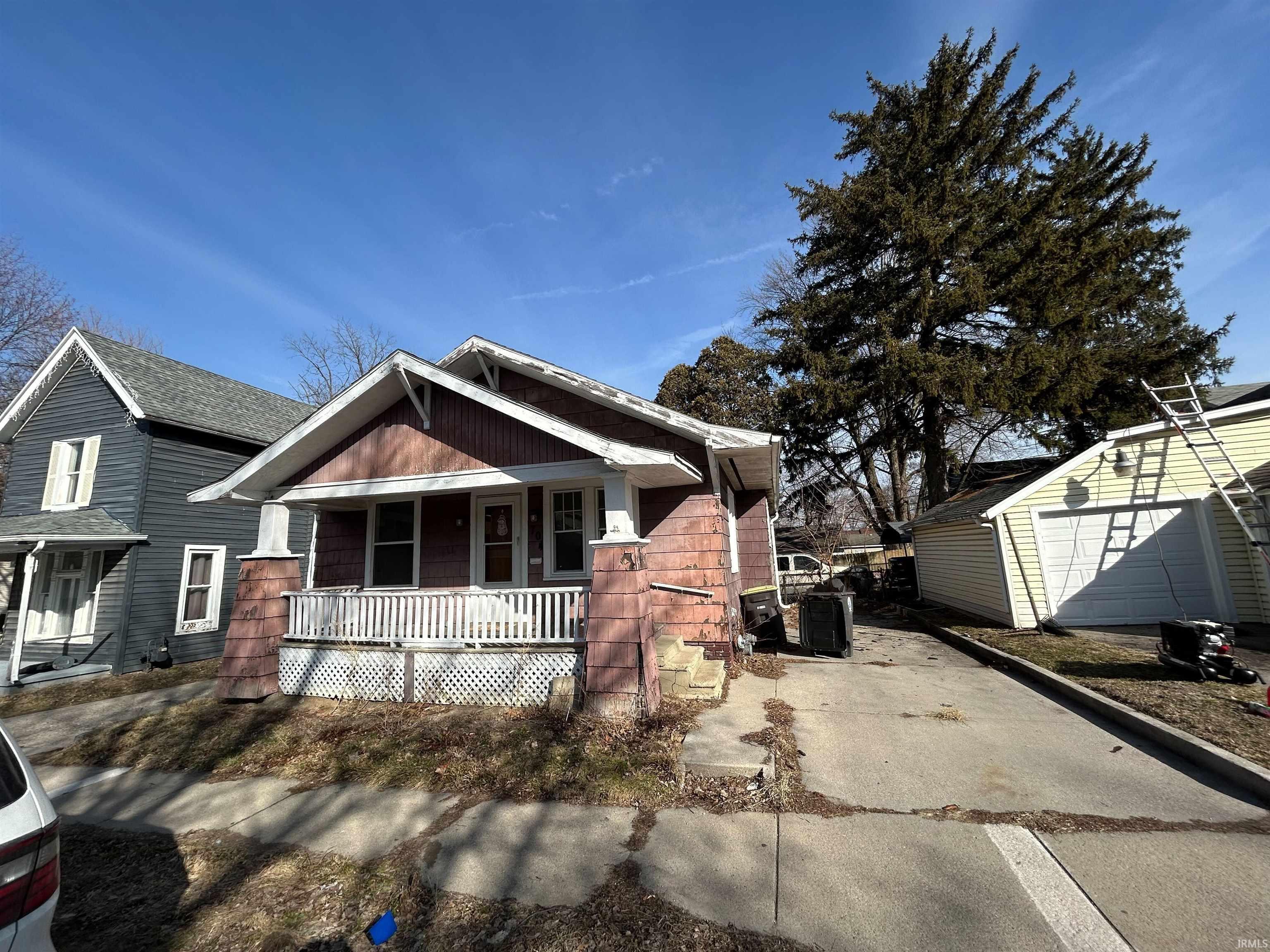 Bungalow-style residence featuring a covered front porch with white railings, a detached garage, and a concrete driveway