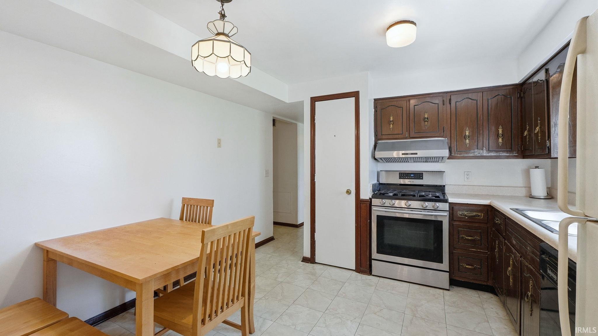 Kitchen featuring dark wood cabinetry, white countertops, and a stainless steel gas range with an overhead exhaust hood