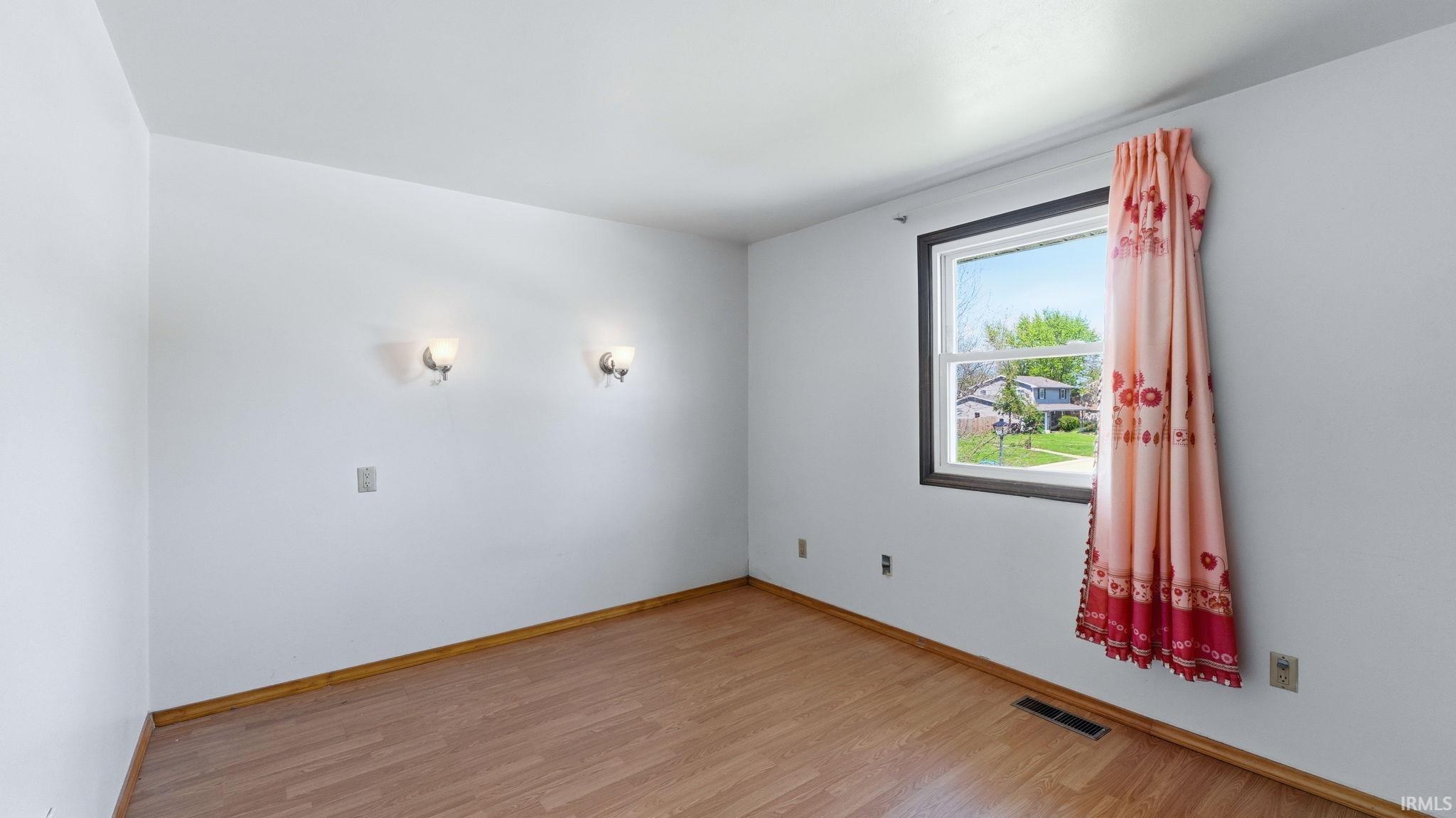 Room featuring light wood-finish flooring, white painted walls, and a double-hung window with dark trim