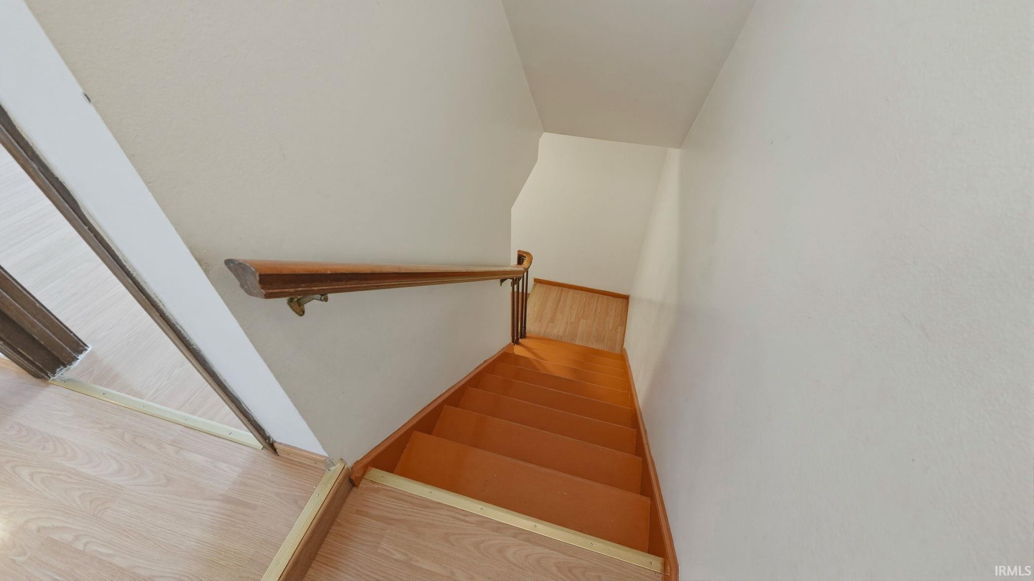 Wood-finish flooring extends from the upper landing, complementing the solid wood handrail with brass accents