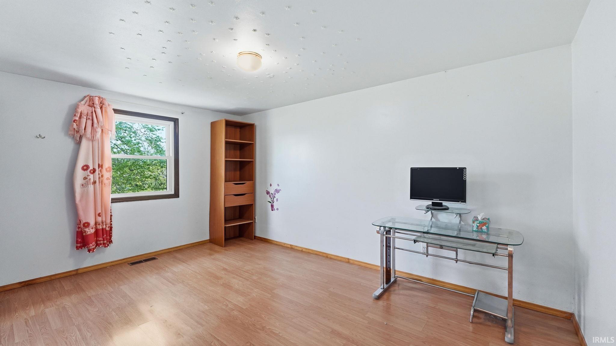 Spacious room featuring wood-finish flooring, white walls, and a window with exterior views