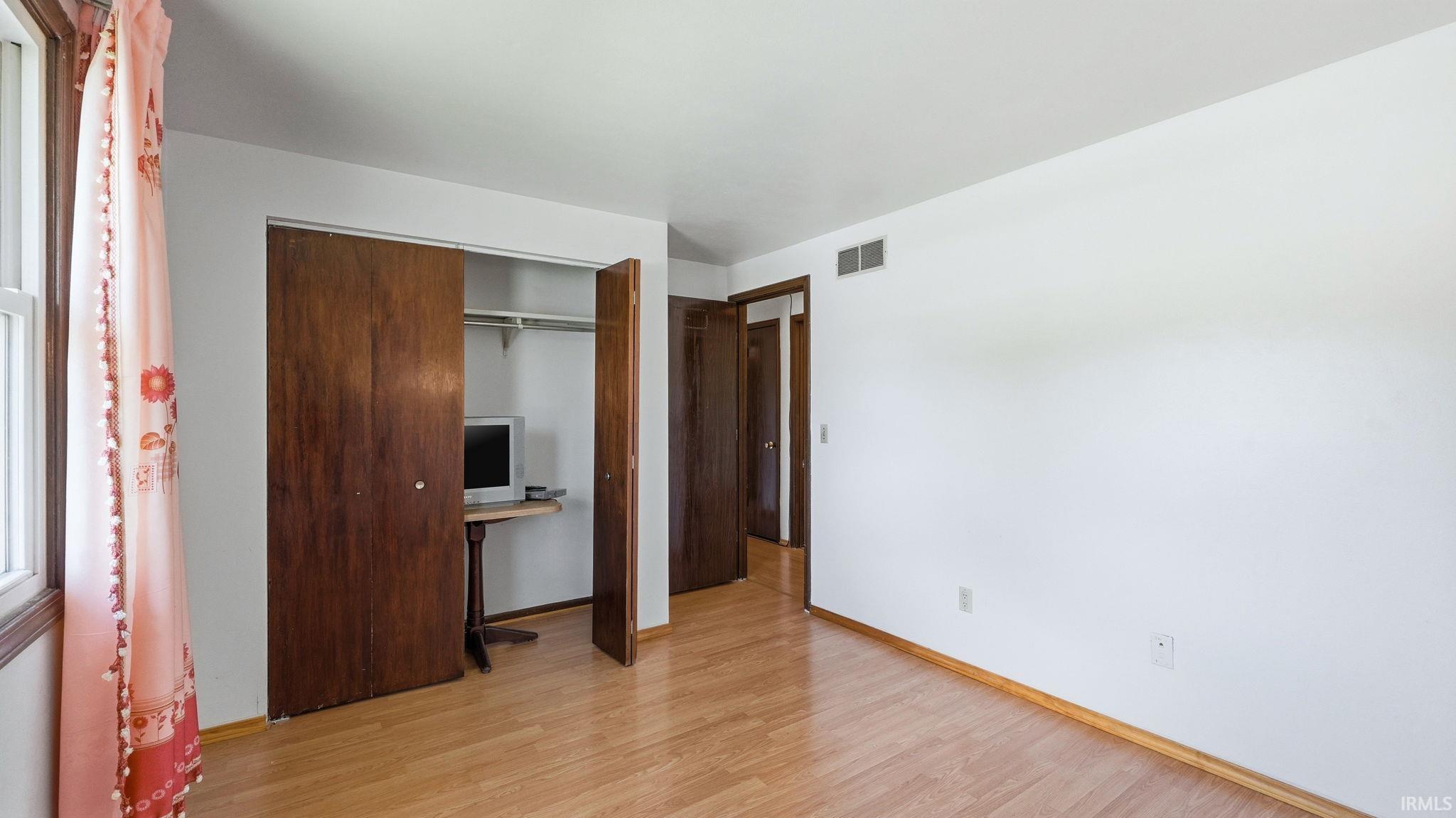 Spacious room featuring wood-finish flooring, white walls, and a window with wood trim