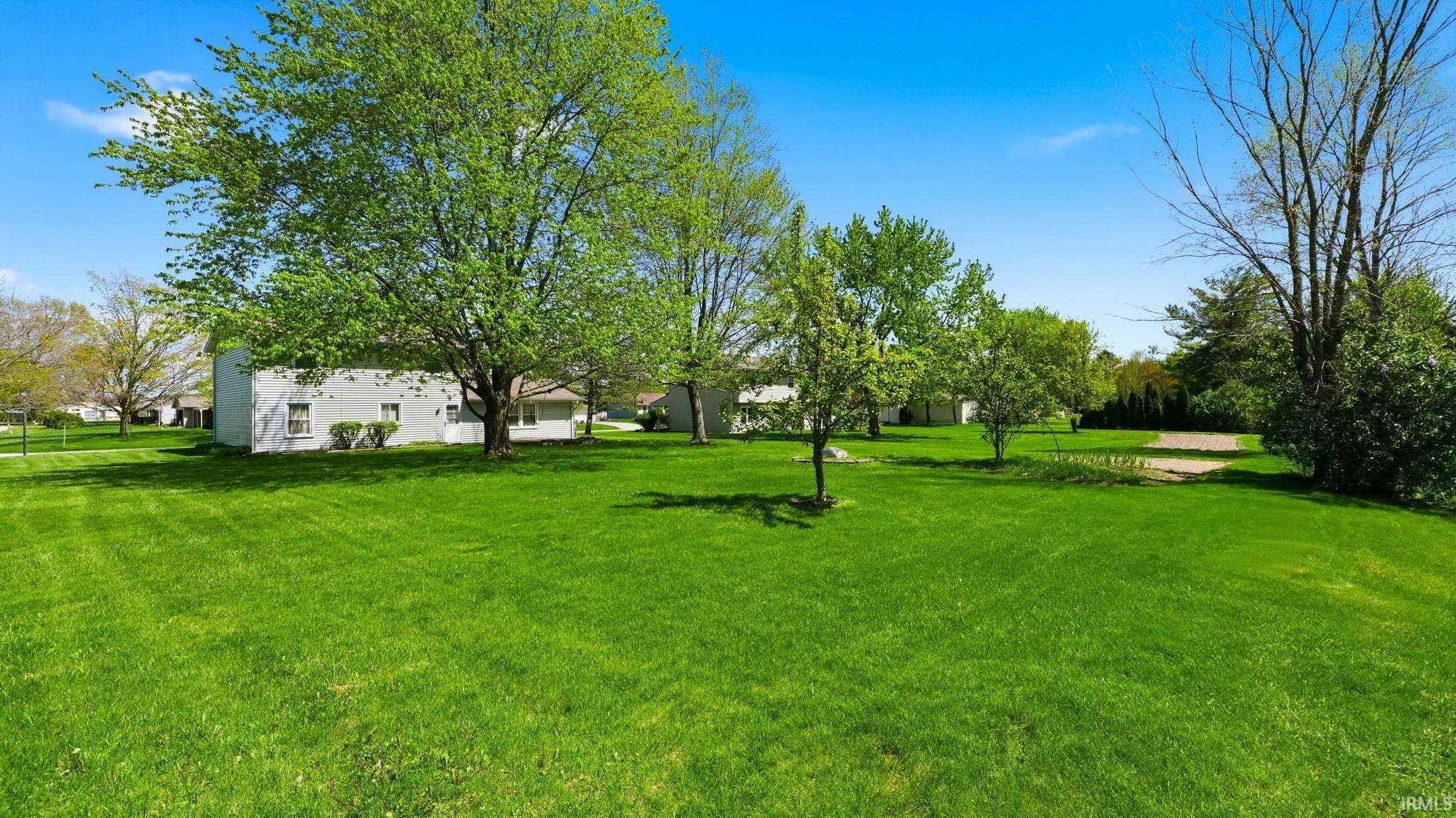 Expansive green lawn with mature trees and a clear sky backdrop