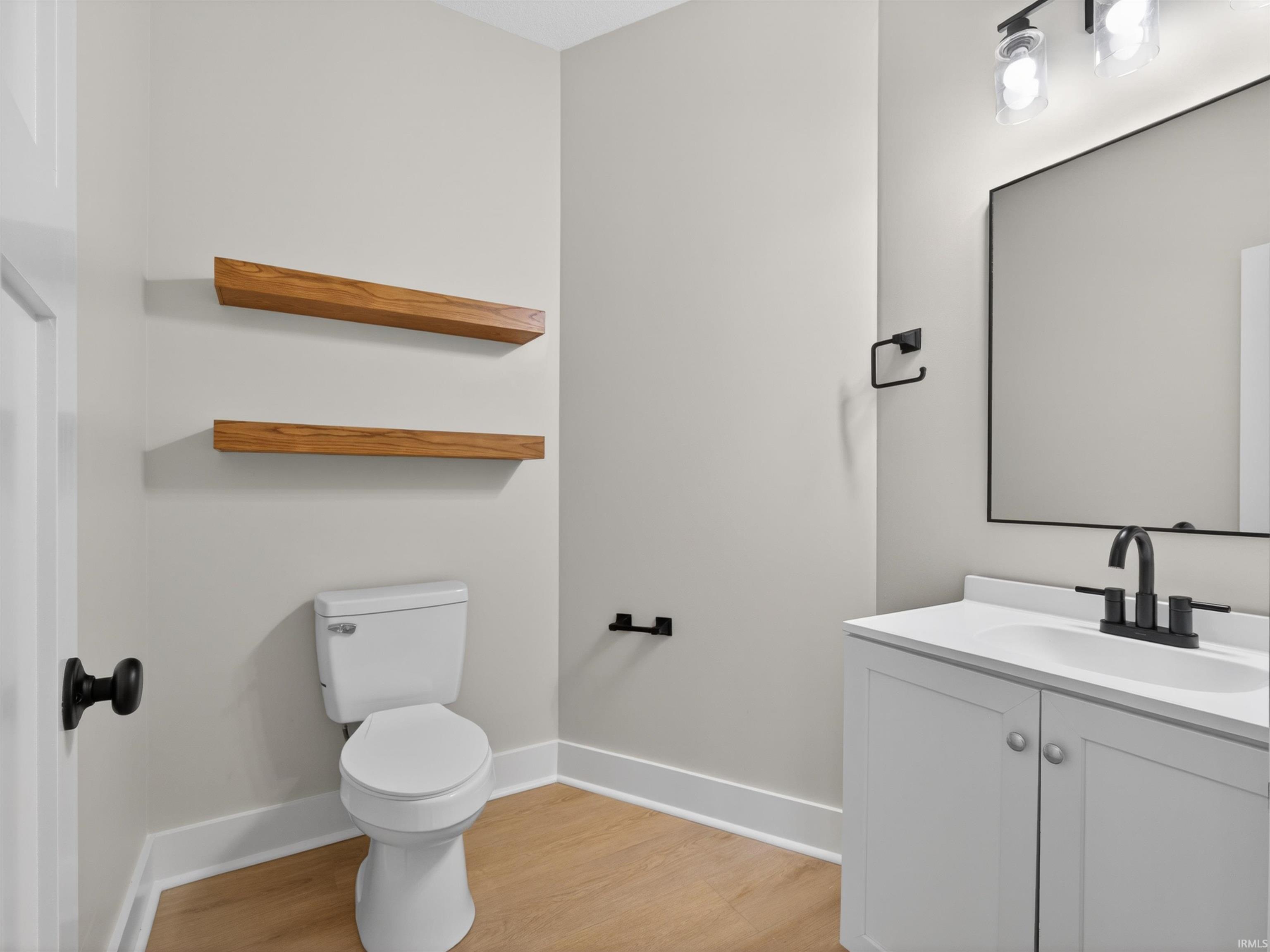 Bathroom featuring a white vanity with integrated sink, matte black fixtures, rectangular mirror, and wood-finish flooring