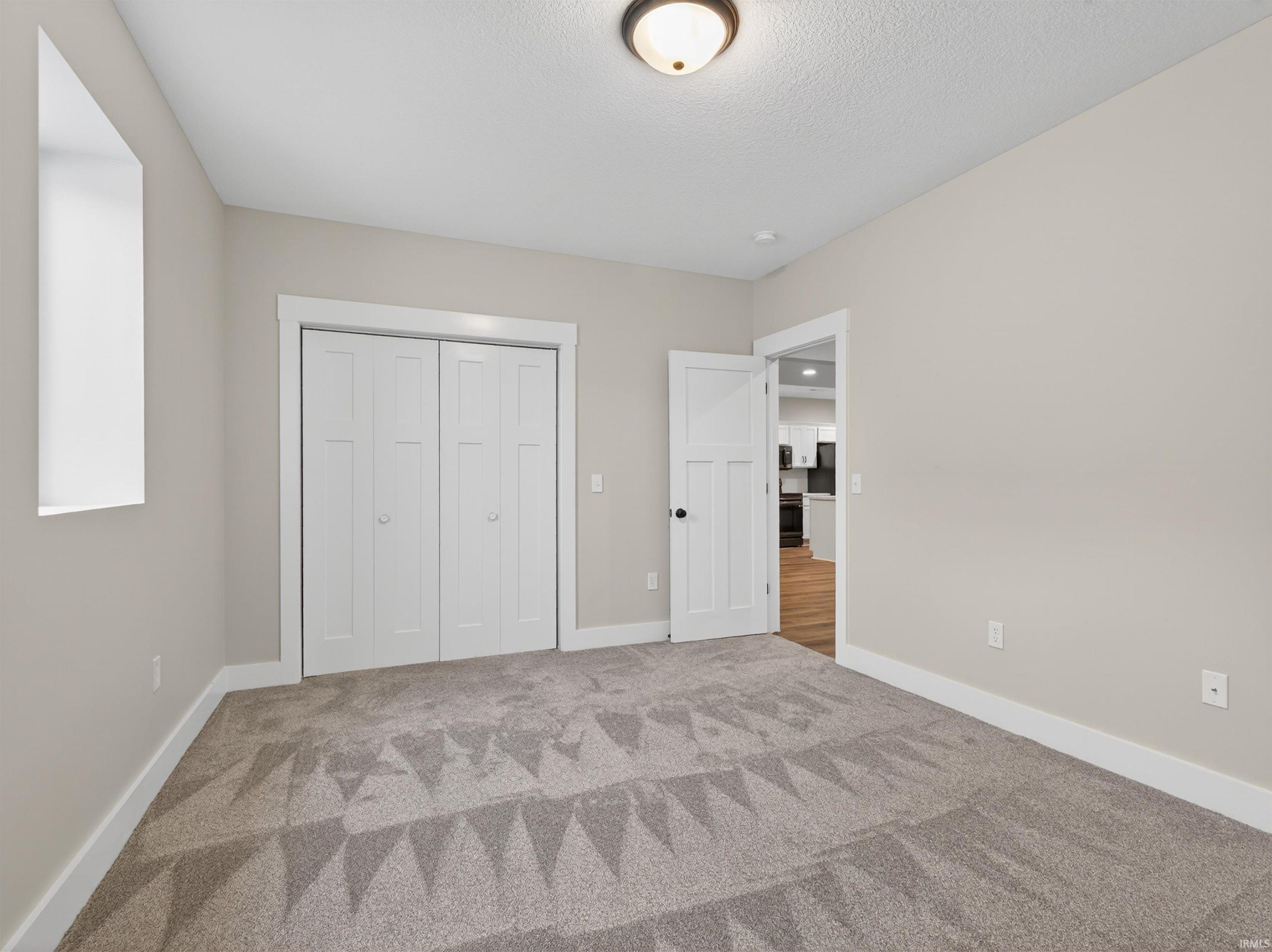 Carpeted room featuring a single window, bi-fold closet doors, a white interior door with black hardware, neutral wall paint, and white trim