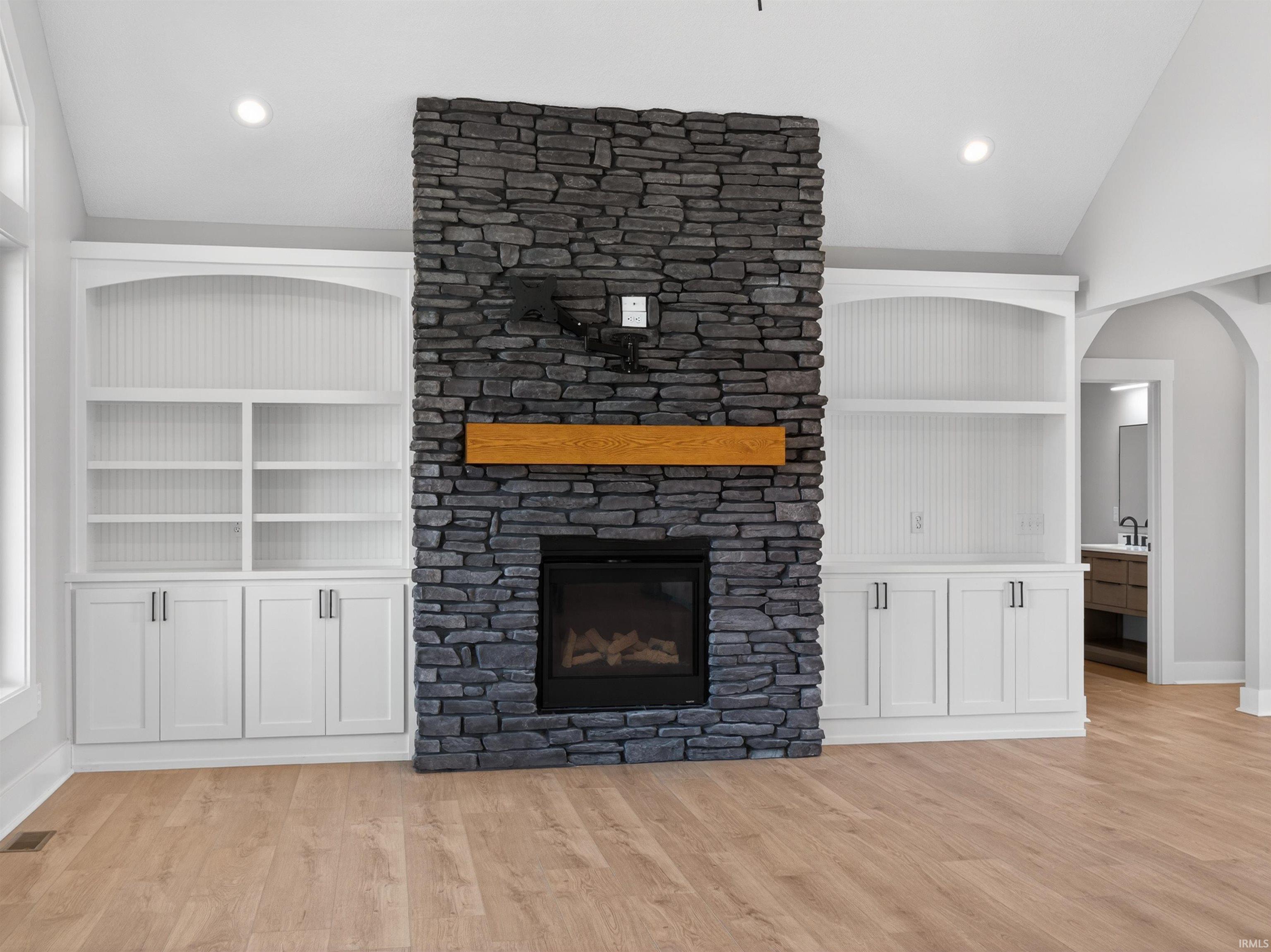 Stone-clad fireplace with a natural wood mantel, flanked by built-in white cabinetry and open shelving