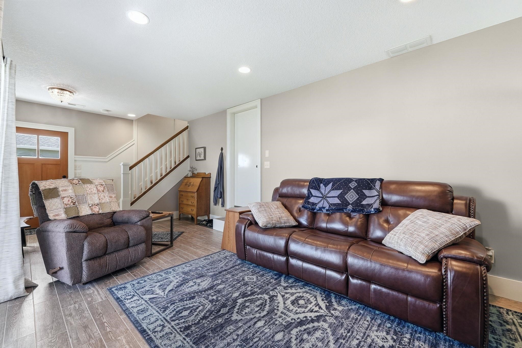 Living area featuring wood-finish flooring, recessed lighting, a wooden staircase with white balusters, and a solid wood front door with glass panels