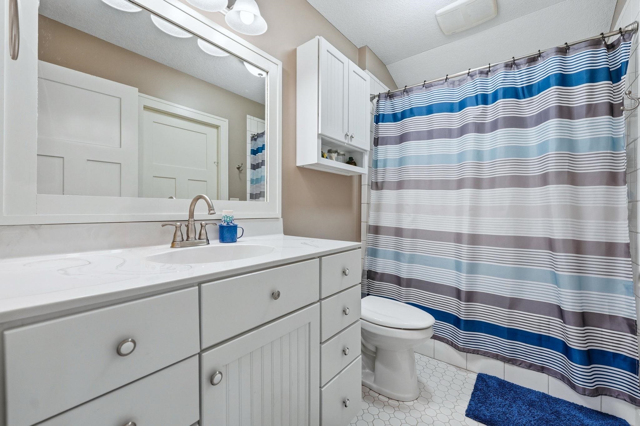 Bathroom featuring a white vanity with a single basin sink, white countertops, built-in cabinetry, and a shower with white tile surround