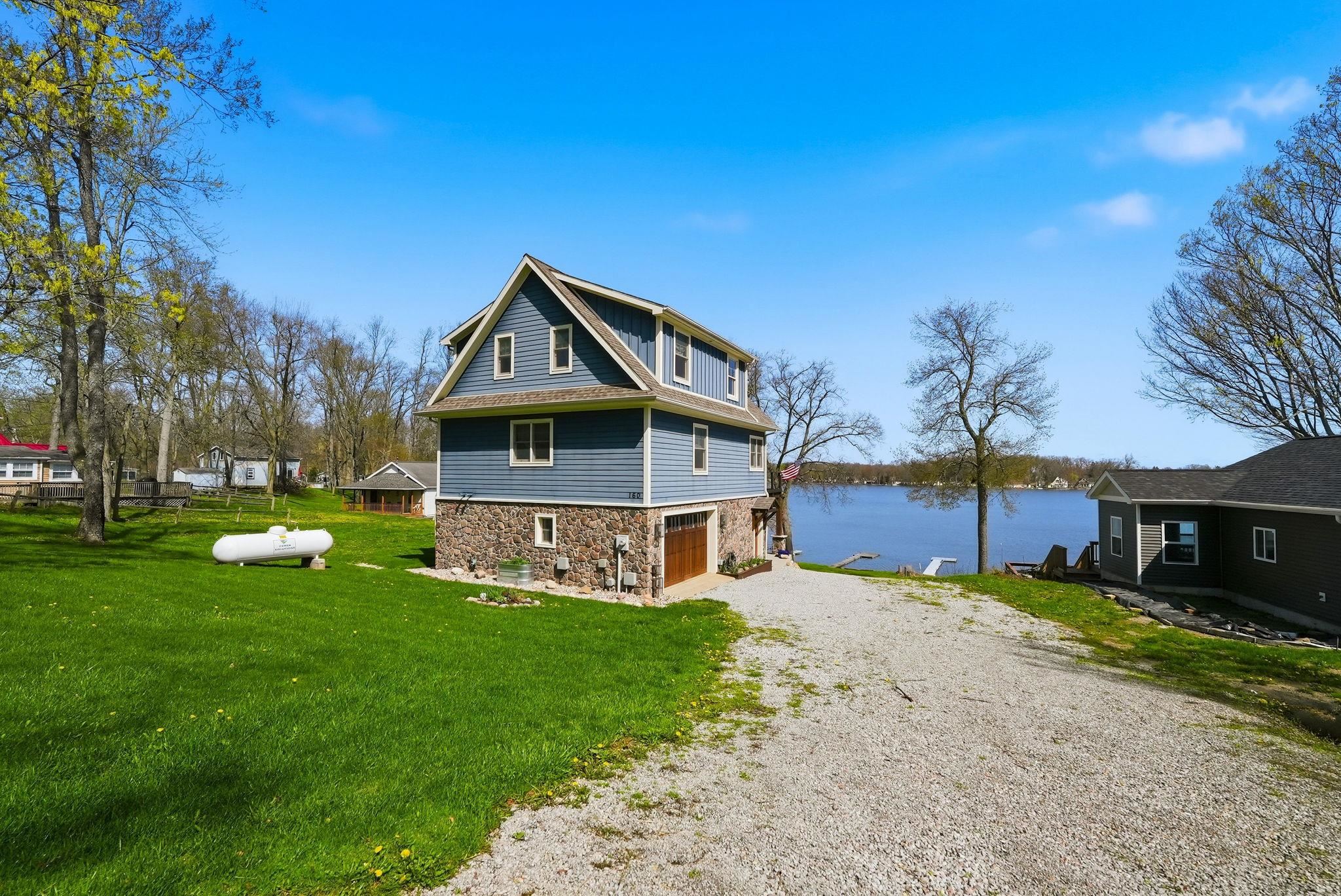 Blue siding residence with a stone-finish lower level, an attached garage, and a gravel driveway