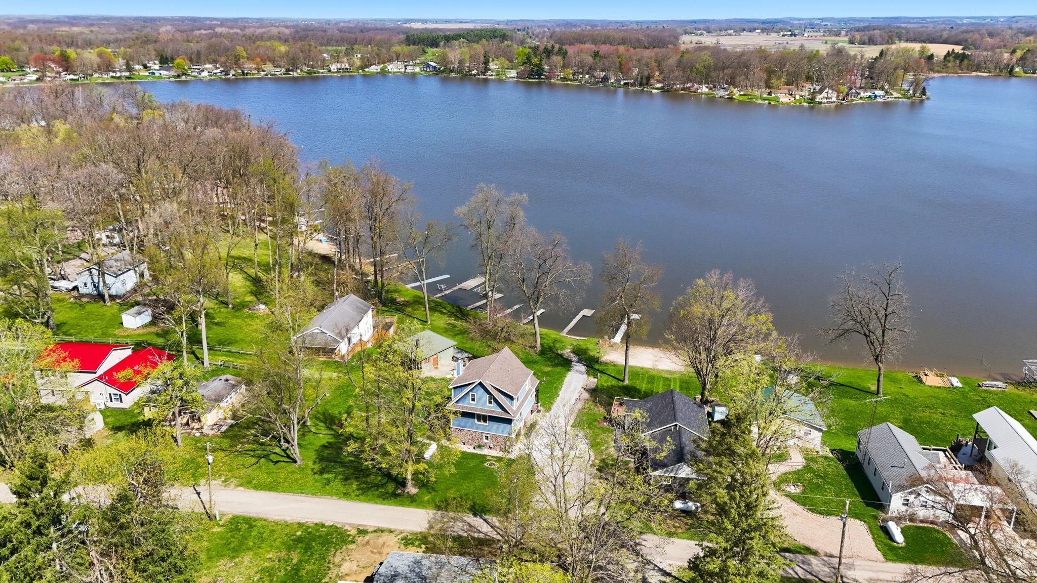 Lakefront property featuring a private dock, expansive green space, mature trees, and a gravel pathway to the water