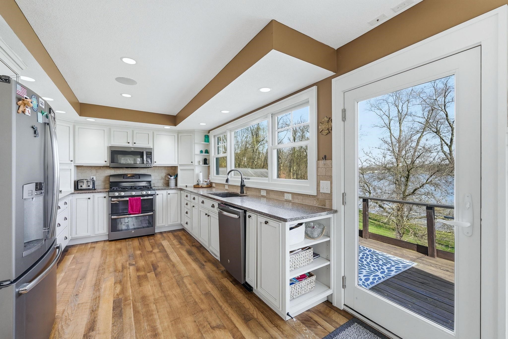 Kitchen featuring white cabinetry, stone-finish countertops, wood-finish flooring, stainless steel appliances, and a full-light door opening to an outdoor deck