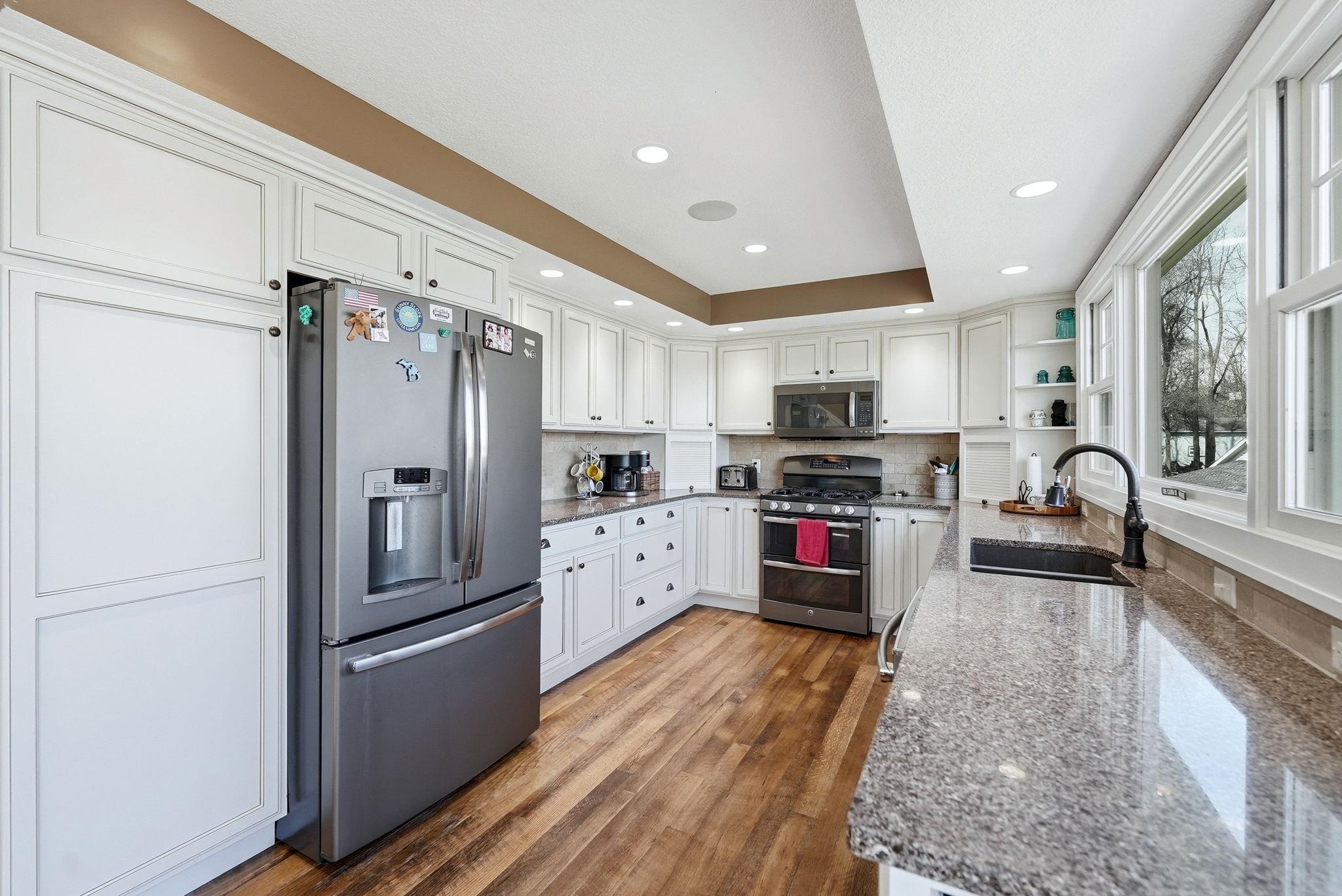 Kitchen featuring white cabinetry, wood-finish flooring, granite countertops, a stainless steel gas range, and a window over the sink