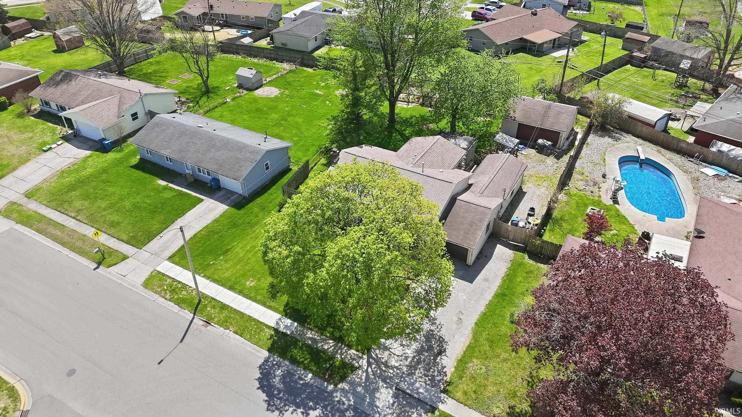 Expansive property featuring a bright blue swimming pool, multiple outbuildings, mature trees, and a concrete driveway