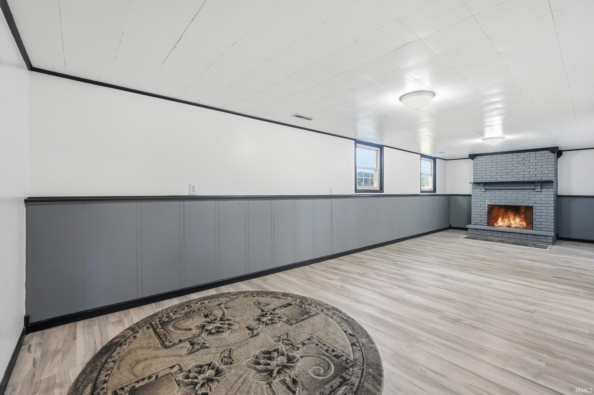 Spacious room featuring a brick fireplace, light wood-finish flooring, and white paneled ceiling