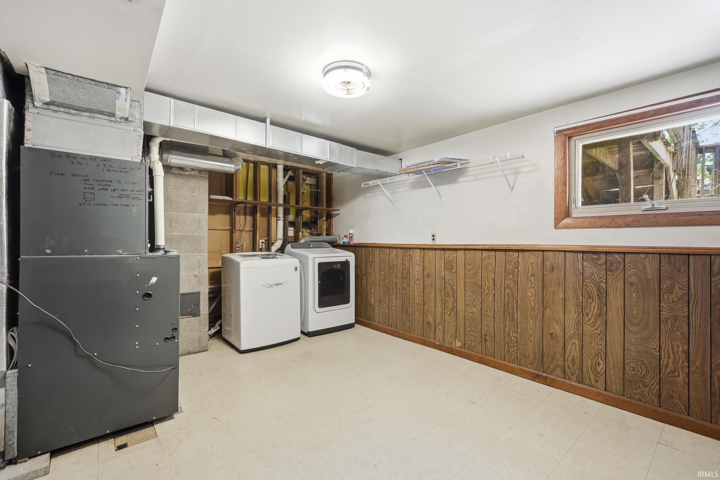 Utility room with washer and dryer, finished with wood paneling and a single window