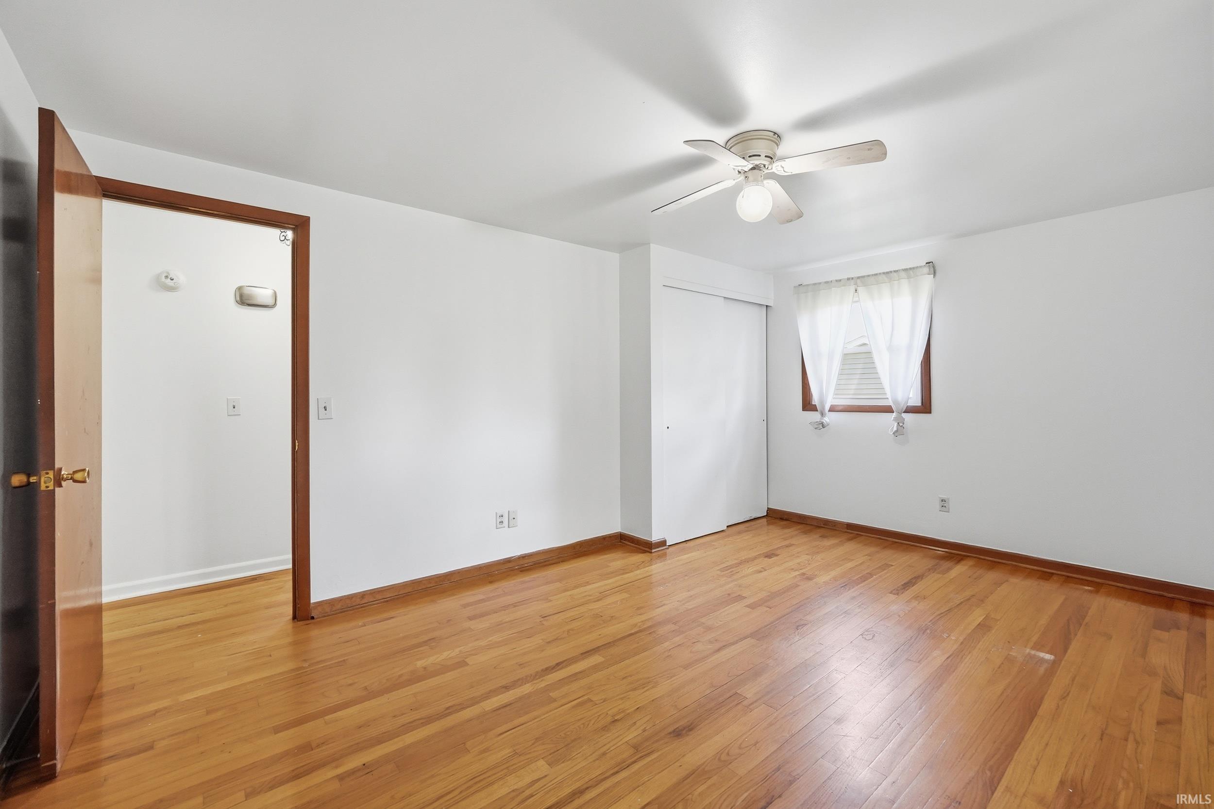 Hardwood flooring throughout featuring white walls and a ceiling fan