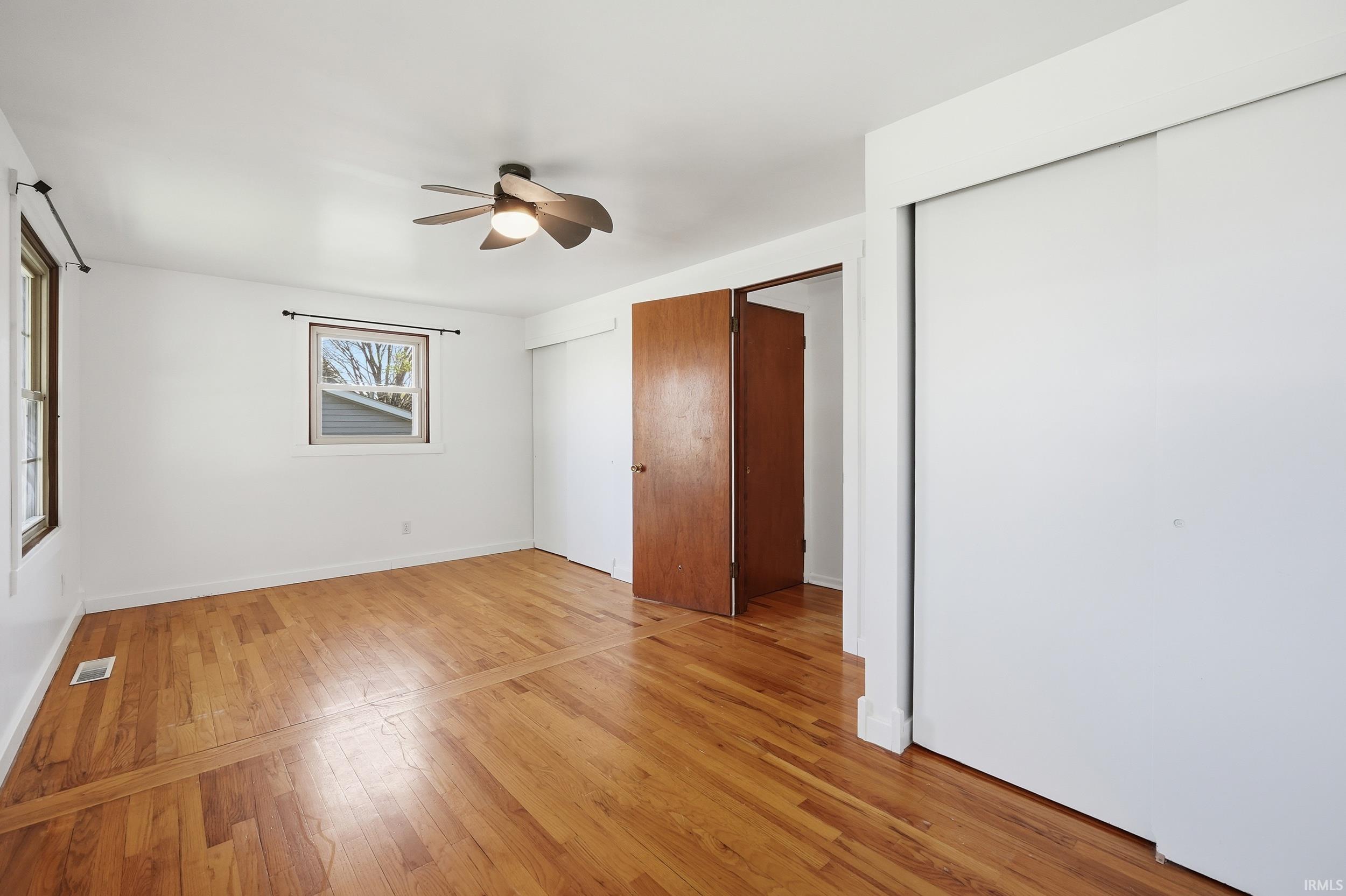 Spacious room featuring wood-finish flooring, two windows, two large closets with sliding doors, and a ceiling fan