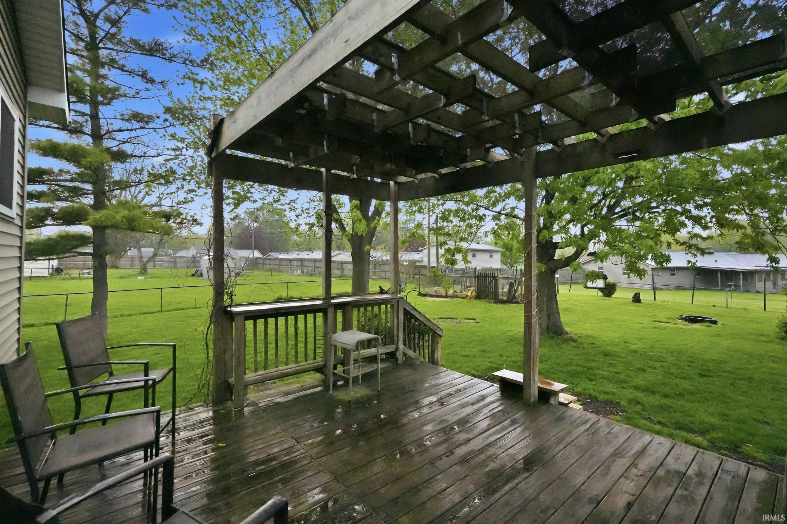 Expansive backyard featuring a wood deck with a pergola, perimeter fencing, and mature trees