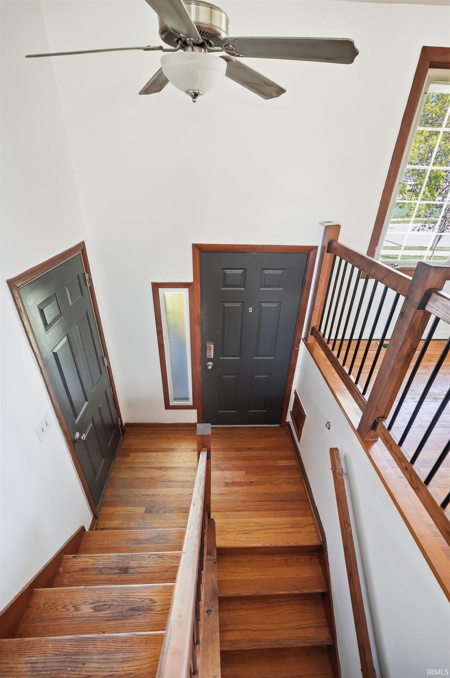 Split-level entry featuring wood-finish flooring, dark-paneled doors, a ceiling fan with integrated lighting, and a large window with white muntins