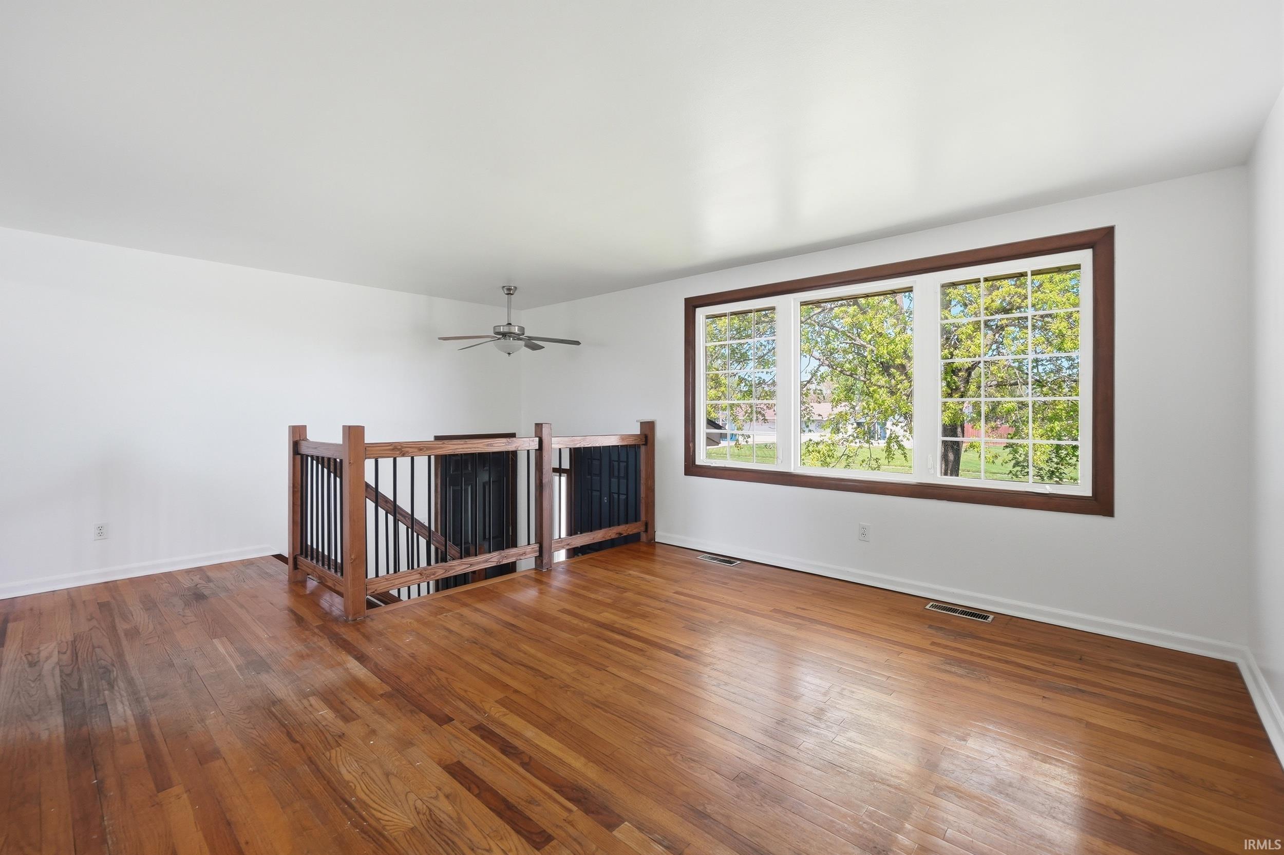 Spacious room featuring hardwood flooring, a multi-pane window with dark trim, and a contemporary ceiling fan