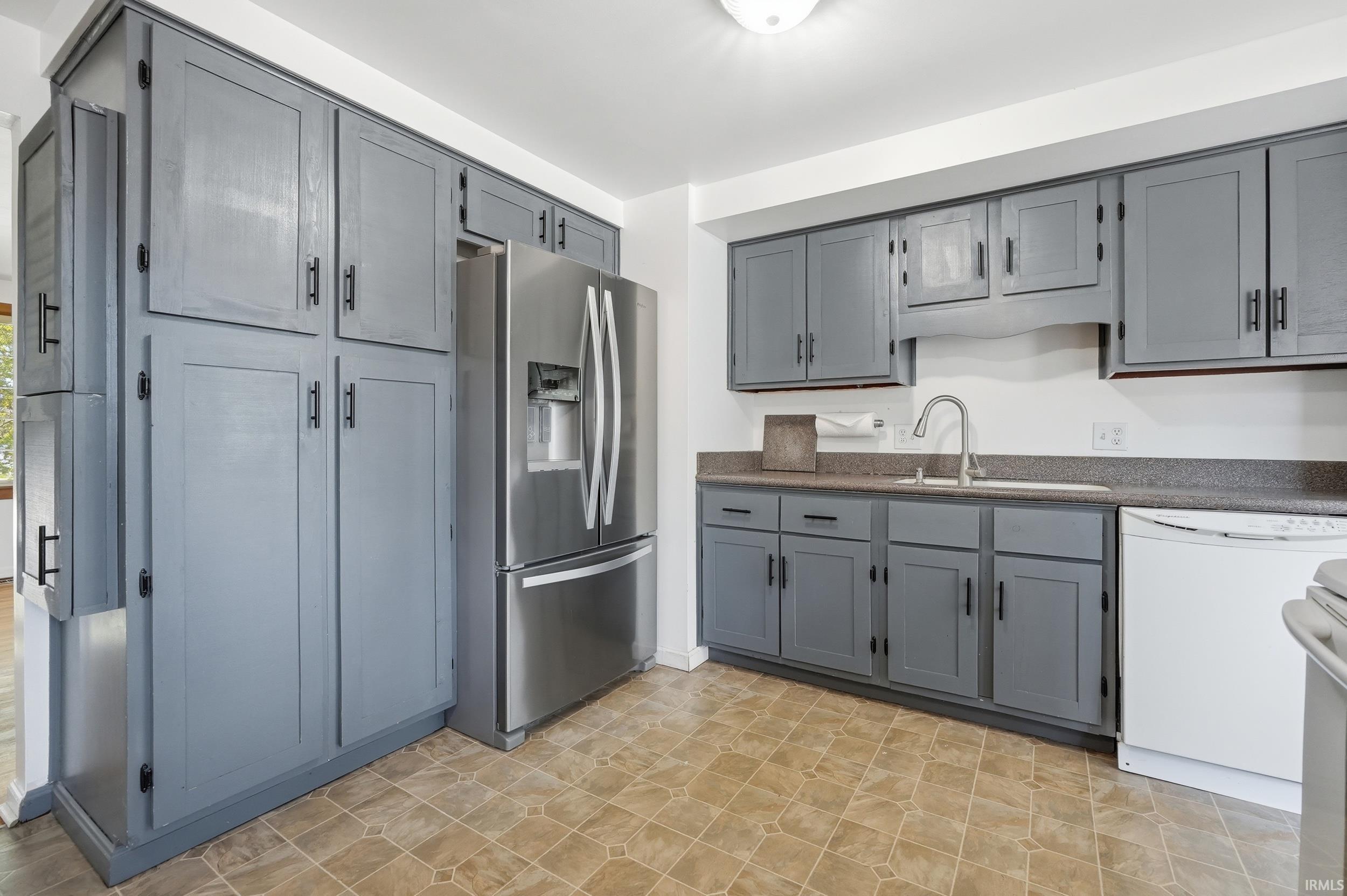 Kitchen featuring gray cabinetry with black hardware, a stainless steel refrigerator, white dishwasher, and a stainless steel sink with a gooseneck faucet