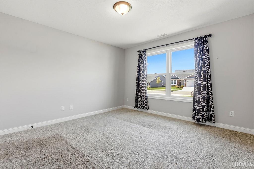 Bright room featuring a large window, neutral gray wall paint, light-toned carpet flooring, white baseboards, and a semi-flush ceiling light fixture