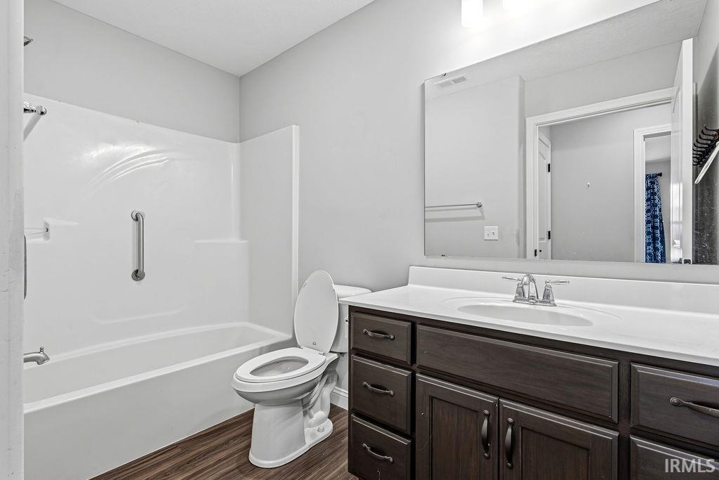 Full bathroom featuring a dark wood-finish vanity with a white countertop and integrated sink, a white toilet, and a combination tub and shower unit with a grab bar