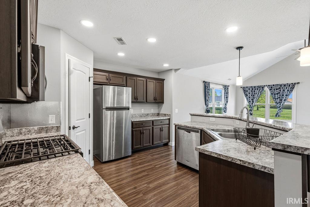 Kitchen featuring dark wood-finish cabinetry, stainless steel appliances, speckled countertops, wood-finish flooring, and recessed lighting