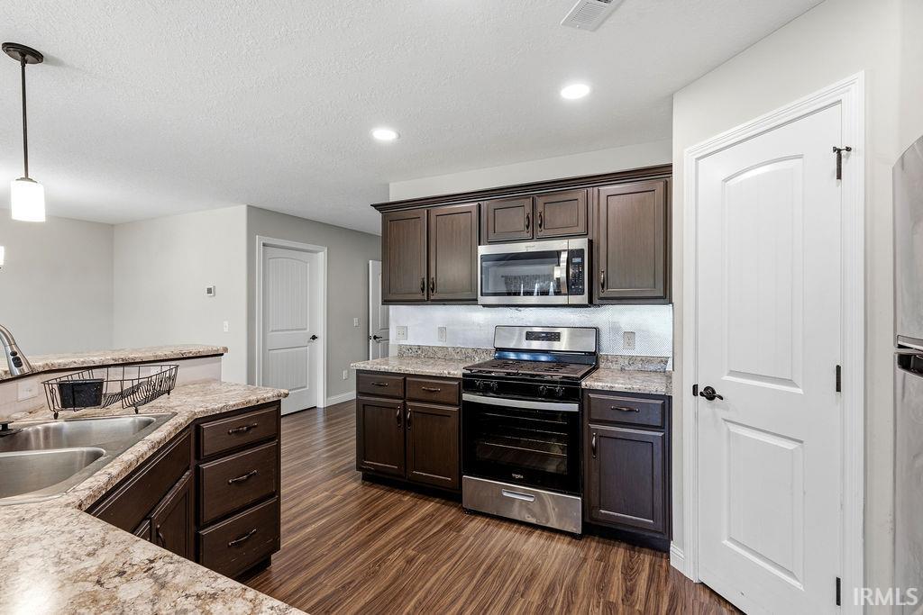 Kitchen featuring dark wood-finish cabinetry, stainless steel appliances, and wood-finish flooring