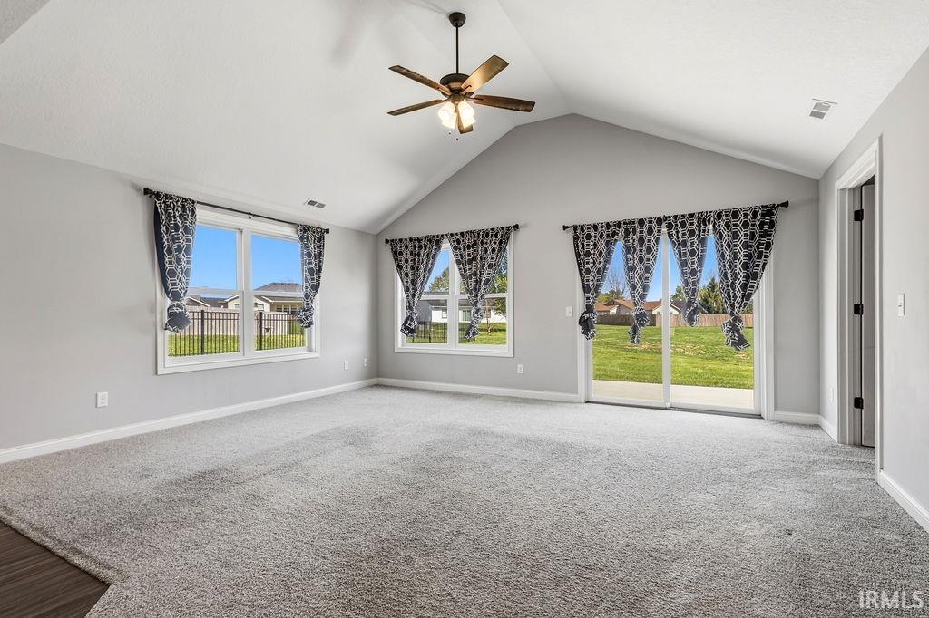 Spacious room featuring a vaulted ceiling with a ceiling fan, plush grey carpeting, and light grey walls