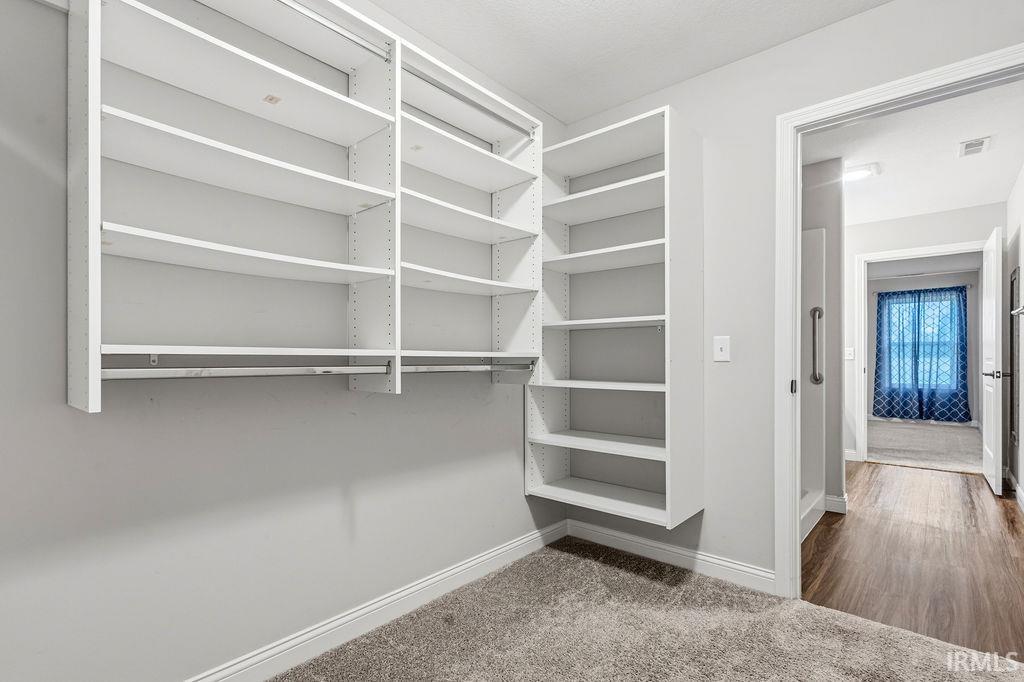 Walk-in closet featuring white built-in shelving, hanging rods, and grey carpeting