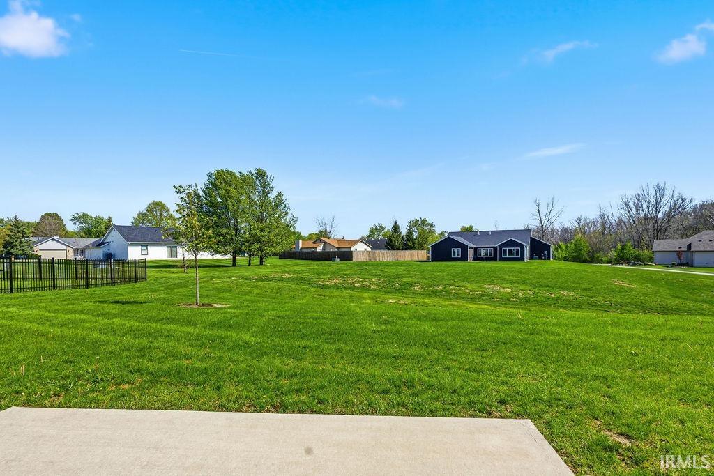 Expansive grass lot featuring a flat concrete pad, mature trees, and a black metal fence