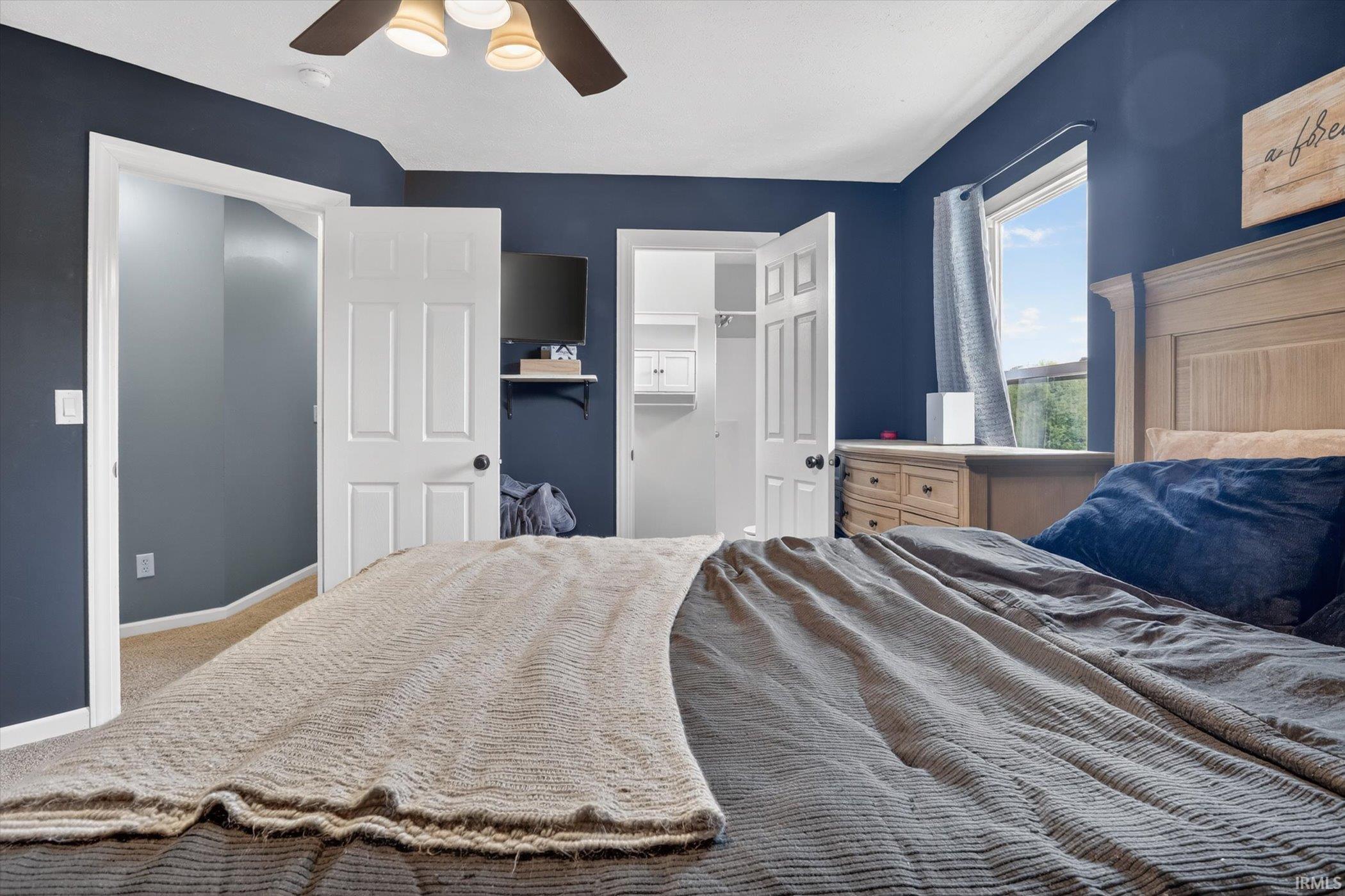 Bedroom featuring dark blue walls, light beige carpeting, and a ceiling fan with integrated lighting