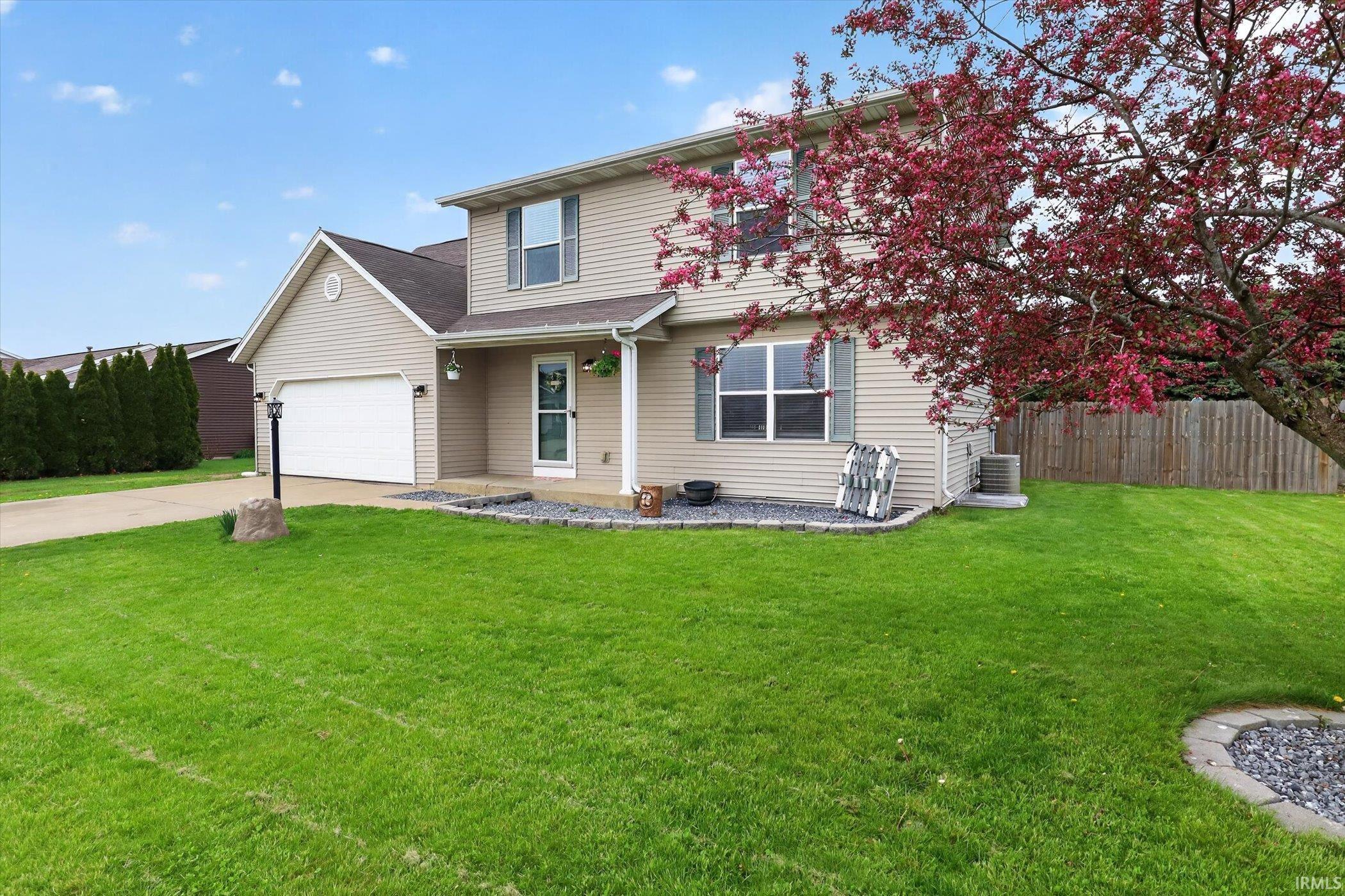 Two-story home featuring tan siding, an attached garage, and a concrete driveway