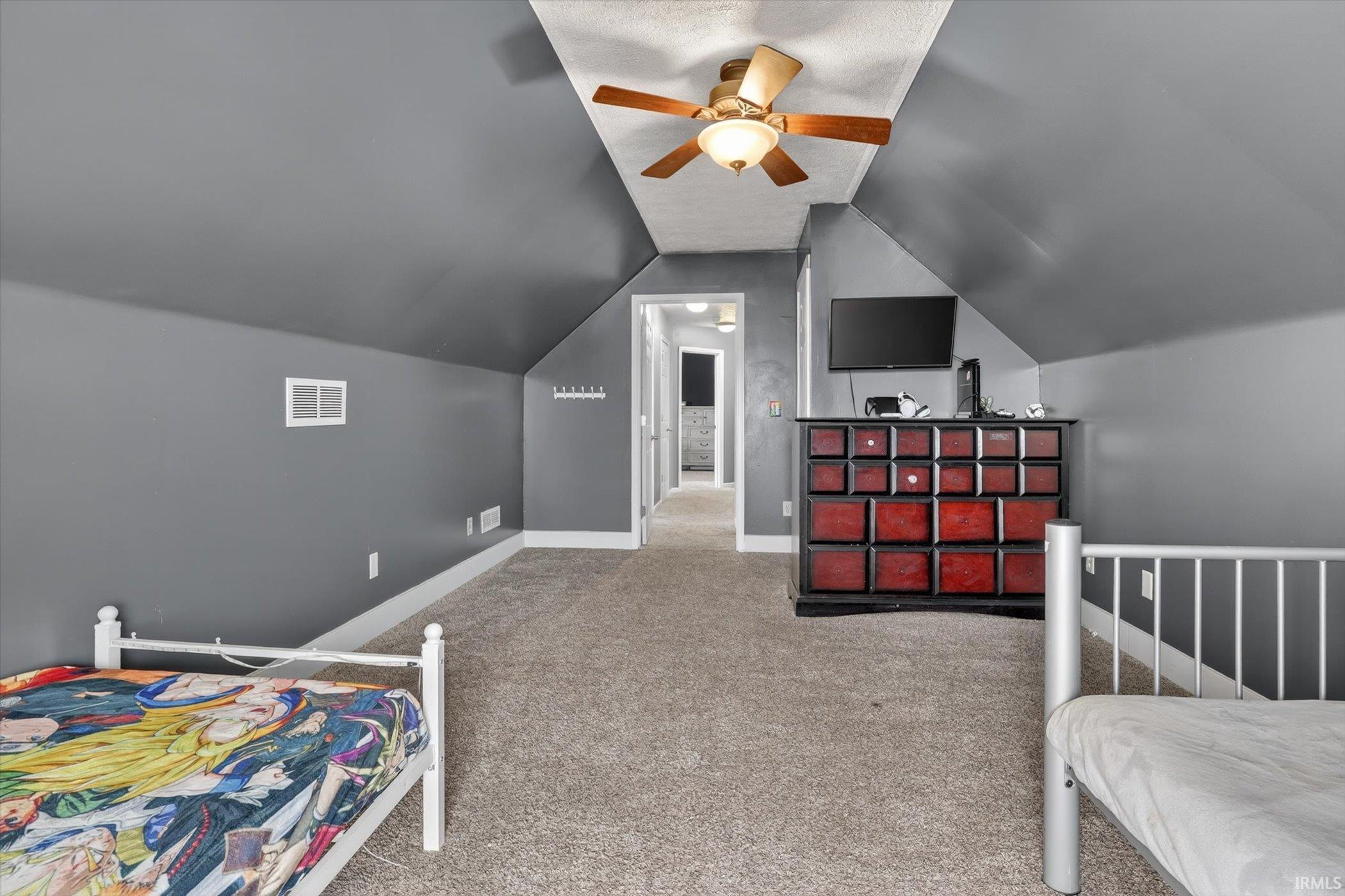 Carpeted room featuring a sloped ceiling, ceiling fan with integrated lighting, gray wall paint, and white trim