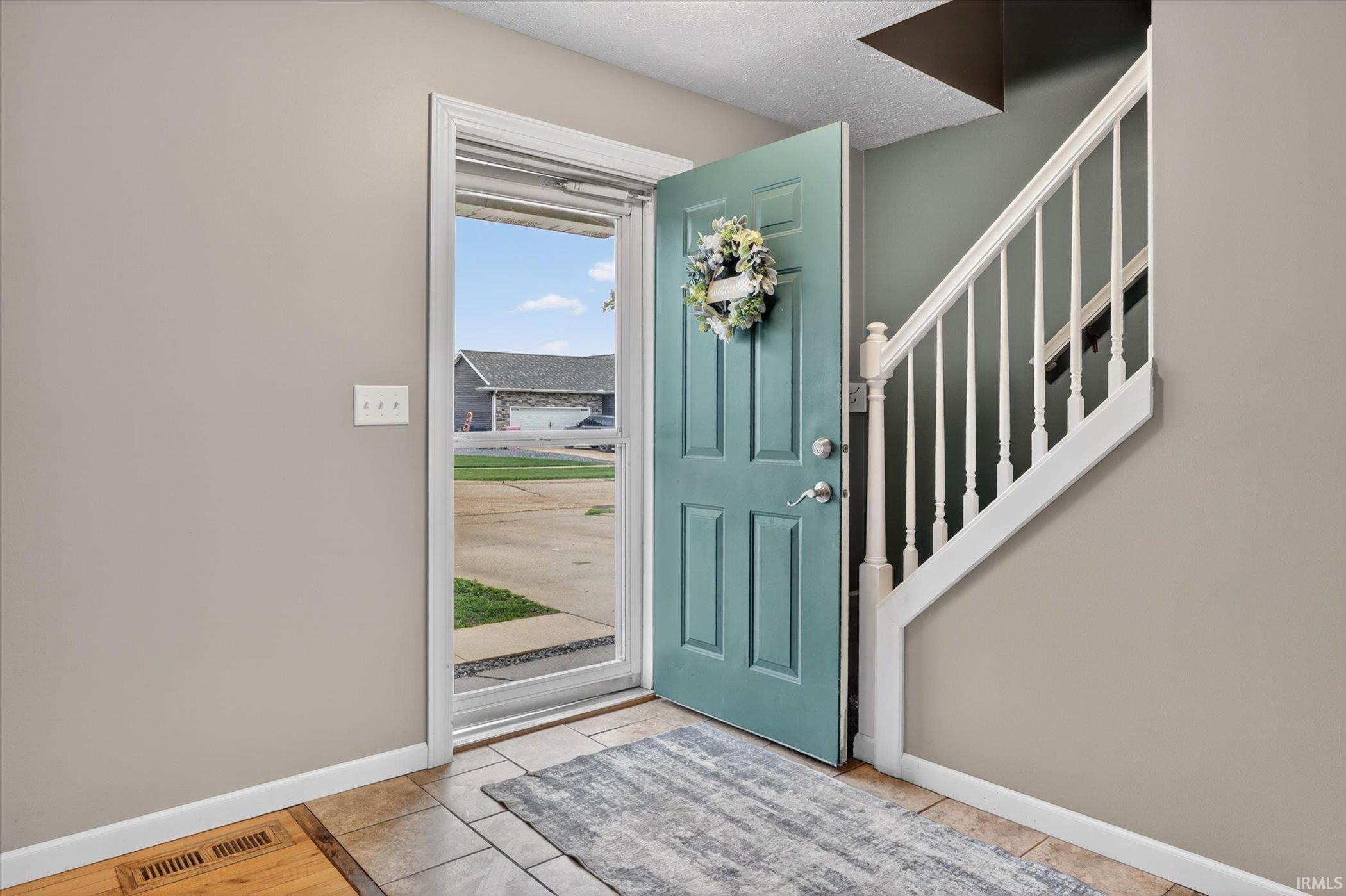 Entryway featuring tile flooring, a staircase with white balusters, and a paneled front door with a storm door