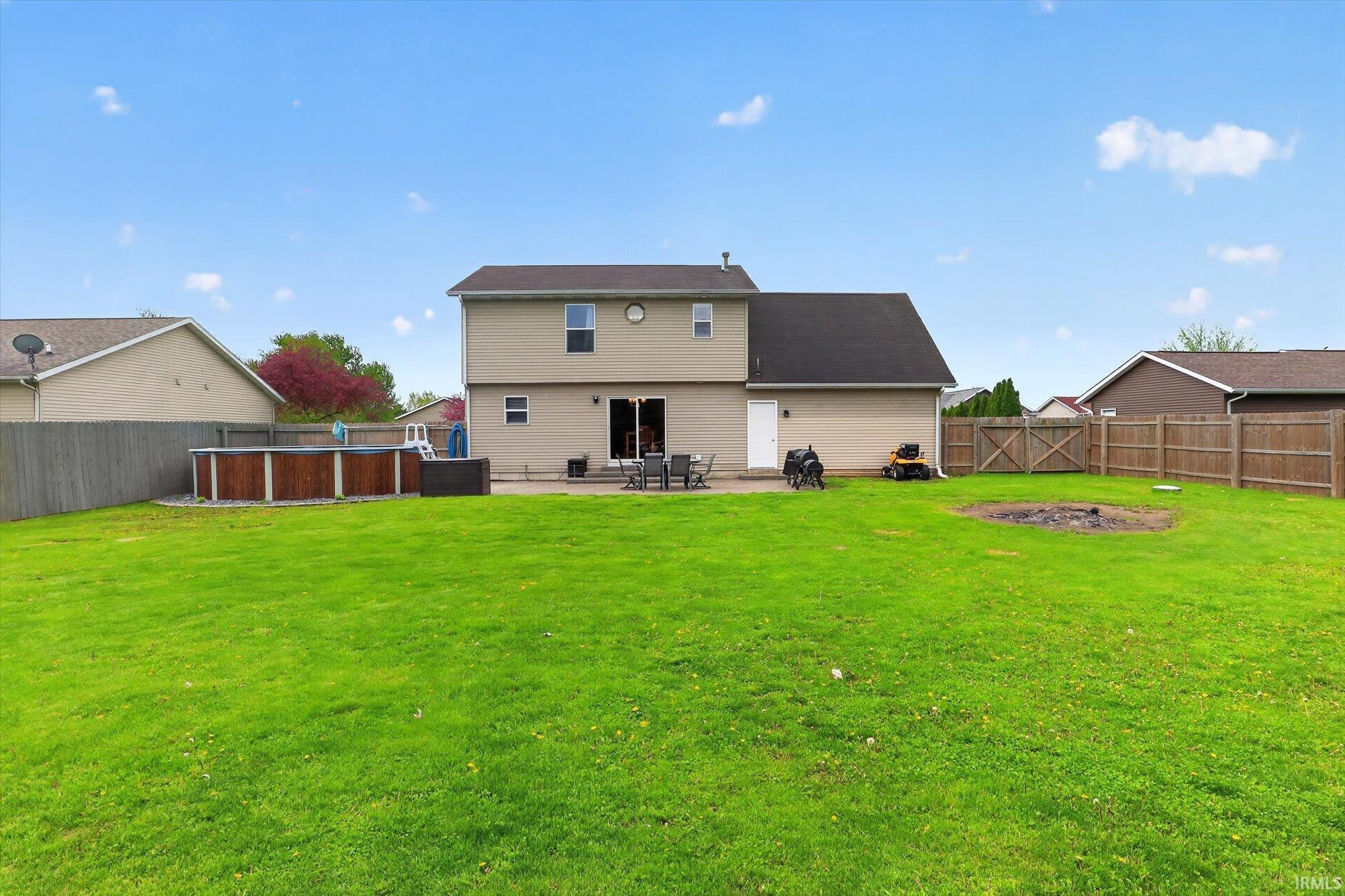 Expansive backyard featuring a large green lawn, an above-ground pool with wood-finish siding, a concrete patio, and a privacy fence