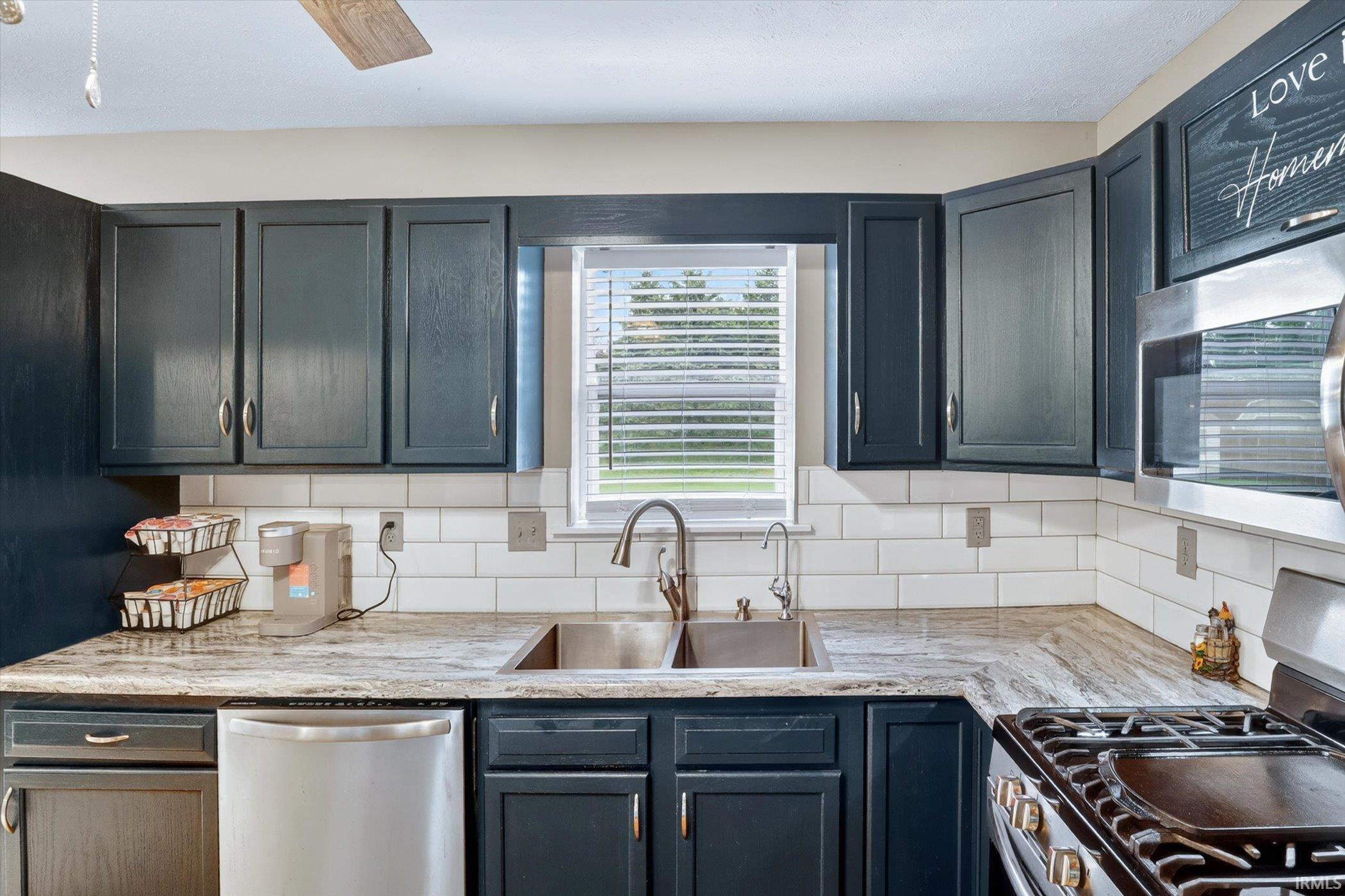 Kitchen featuring dark cabinetry, light countertops, subway tile backsplash, stainless steel appliances, and a window above the sink