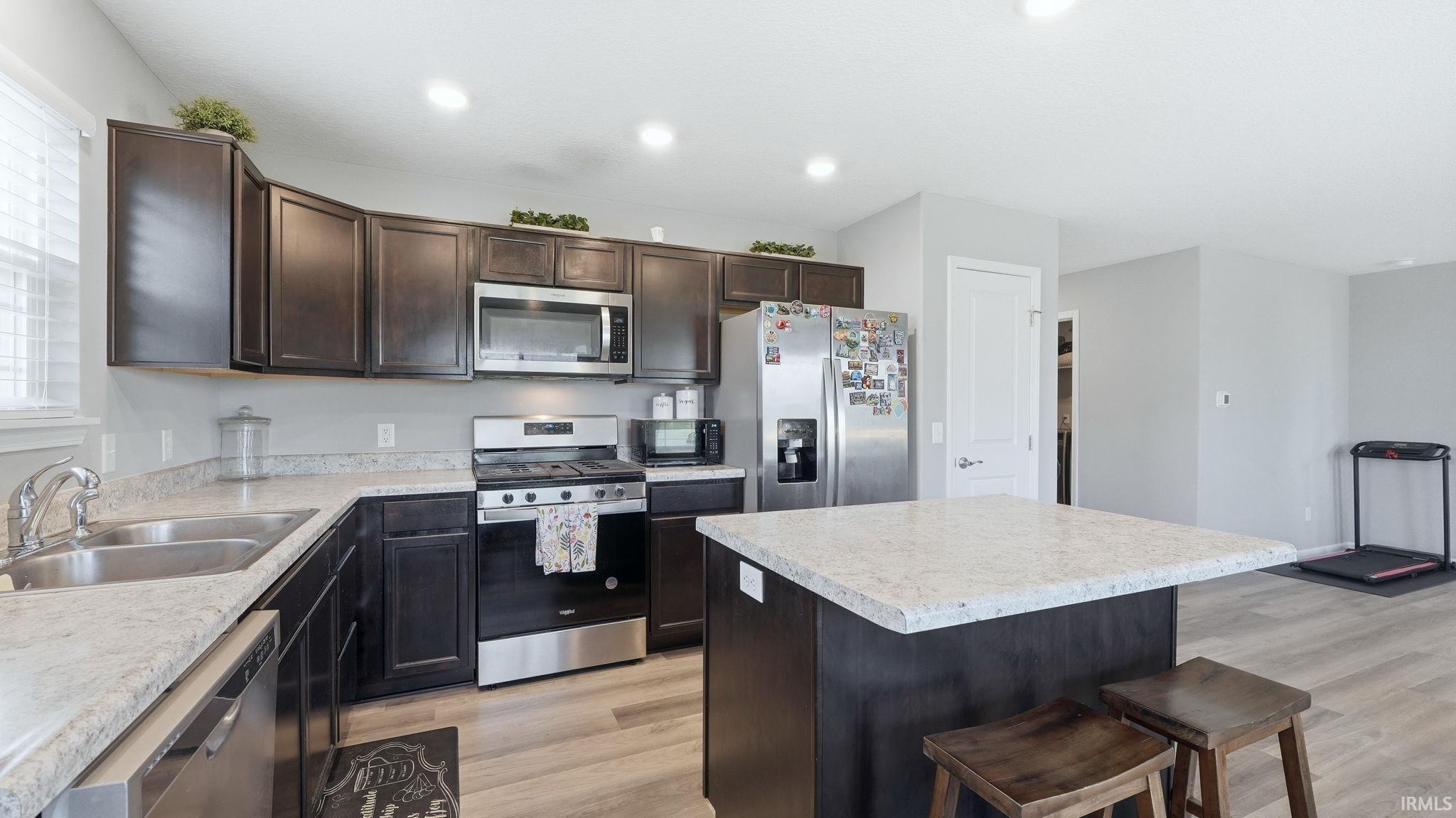 Kitchen featuring dark wood cabinetry, light-toned countertops, stainless steel appliances, and a central island