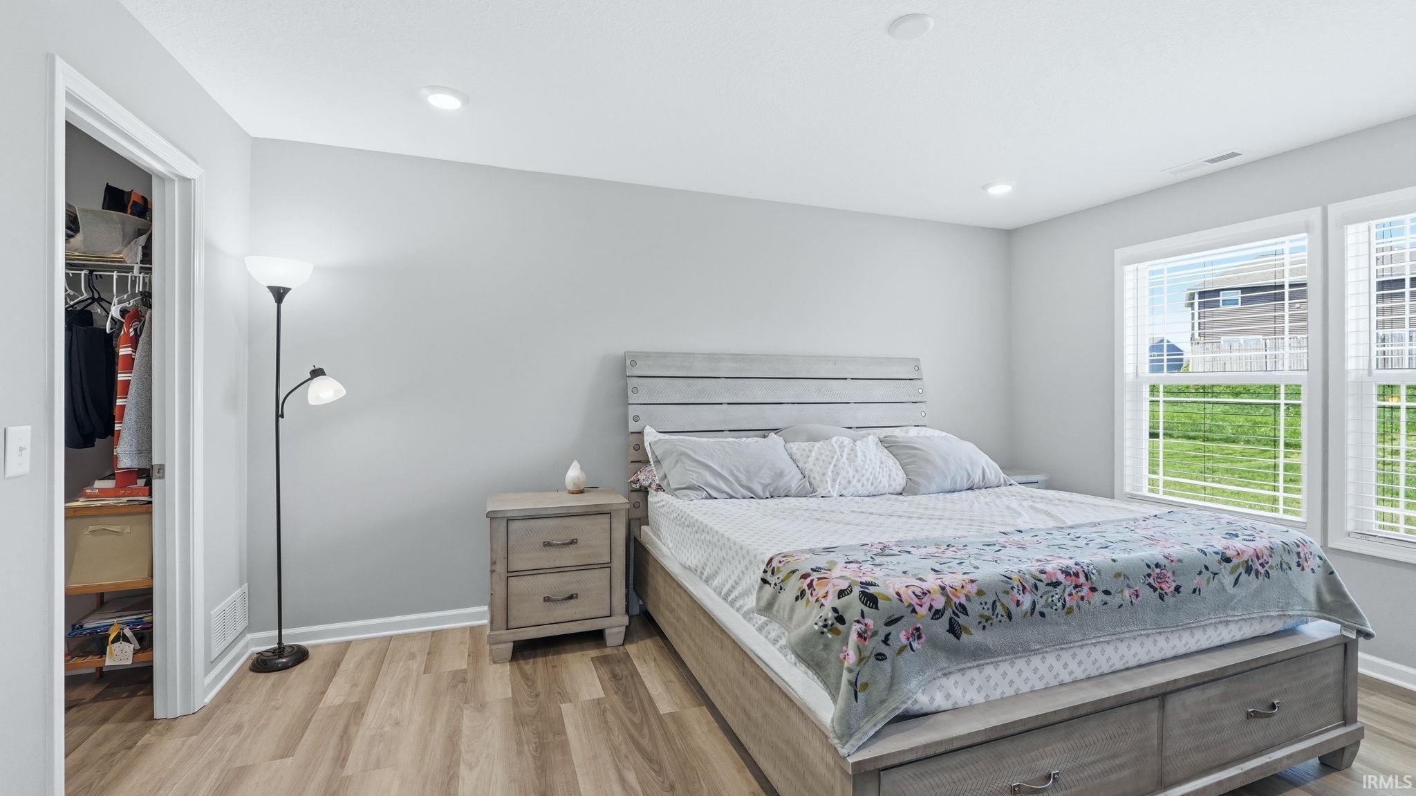 Spacious bedroom featuring light wood-finish flooring, light gray wall paint, and white trim