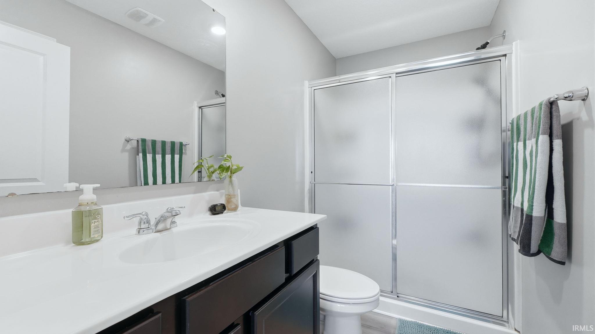 Bathroom featuring a dark wood-finish vanity with a white countertop and integrated sink, a large wall-mounted mirror, a toilet, and a shower with frosted glass sliding doors
