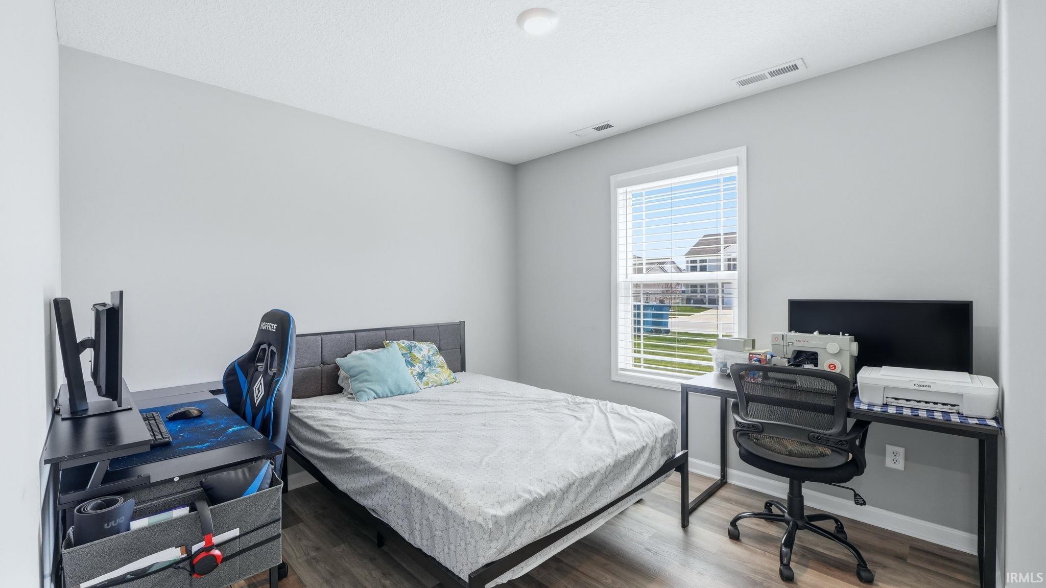 Bedroom featuring neutral gray walls, wood-finish flooring, and a single window with white blinds