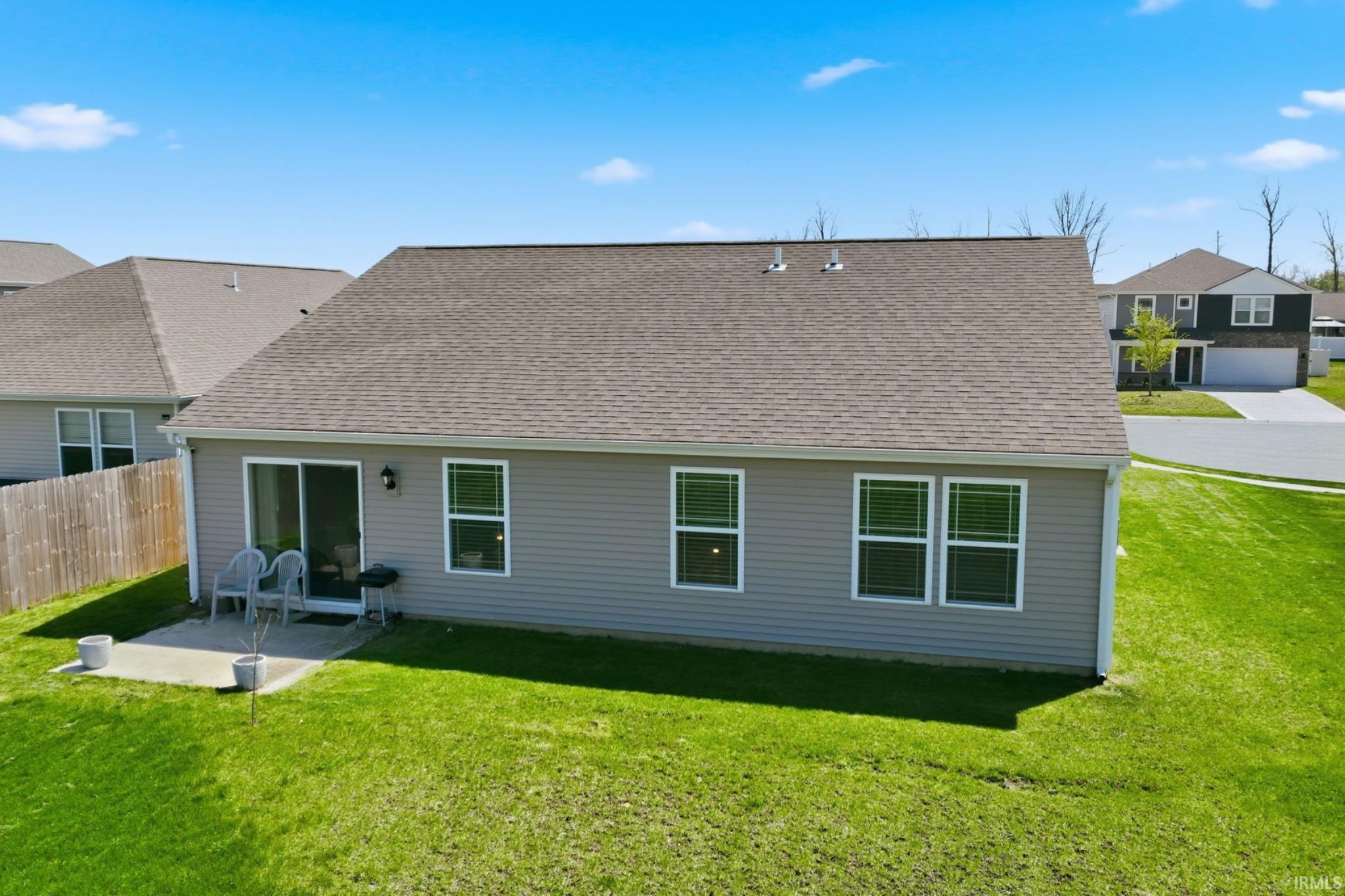 Rear exterior featuring gray siding, a sliding glass door, multiple windows, a concrete patio, and a shingle roof