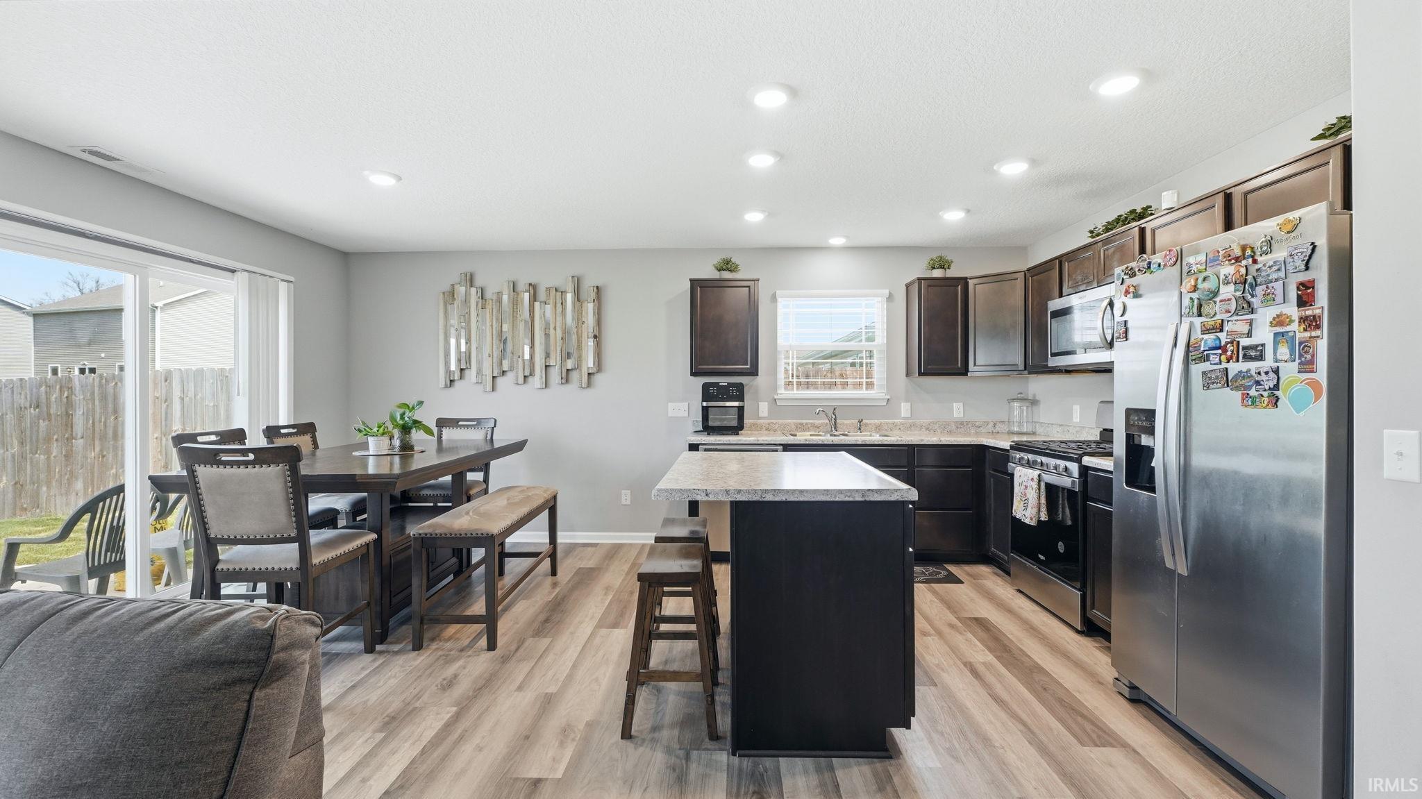 Open-concept kitchen and dining area featuring wood-finish flooring, dark wood cabinetry, a center island with bar seating, and stainless steel appliances