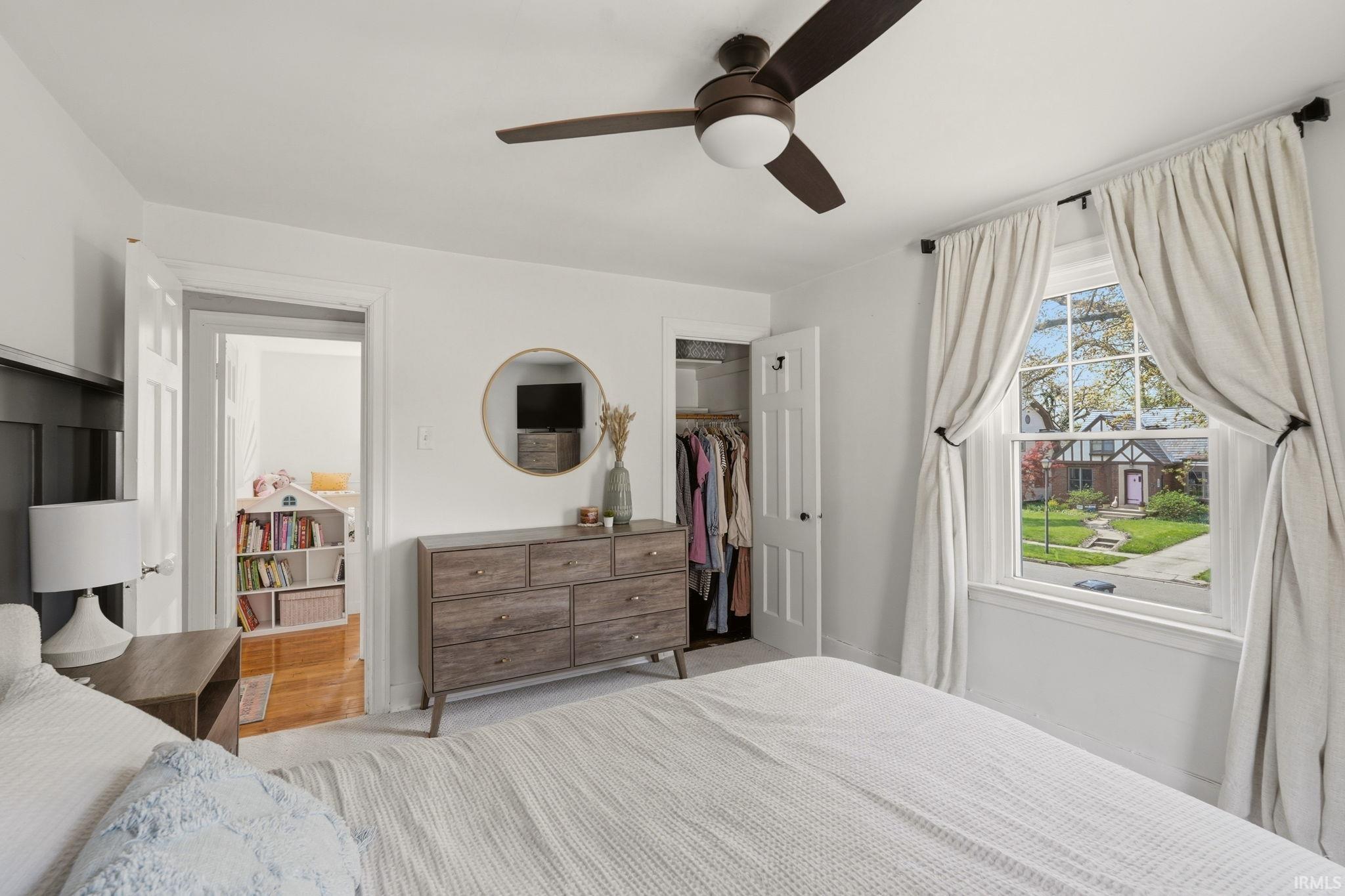 Bedroom featuring white walls, a wood-finish ceiling fan with integrated lighting, a double-hung window with white trim, and an open closet
