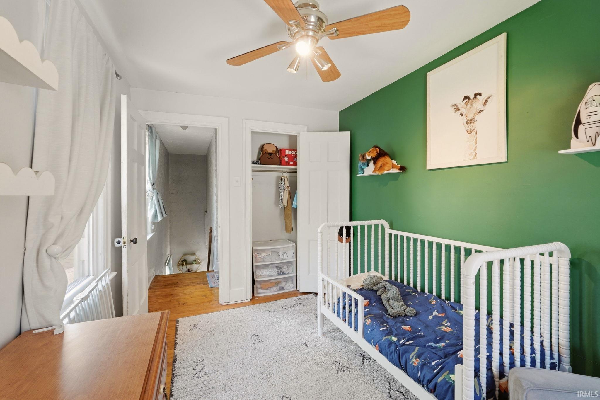 Bedroom featuring a green accent wall, wood-finish flooring, a ceiling fan with light fixture, and an open closet with built-in shelving