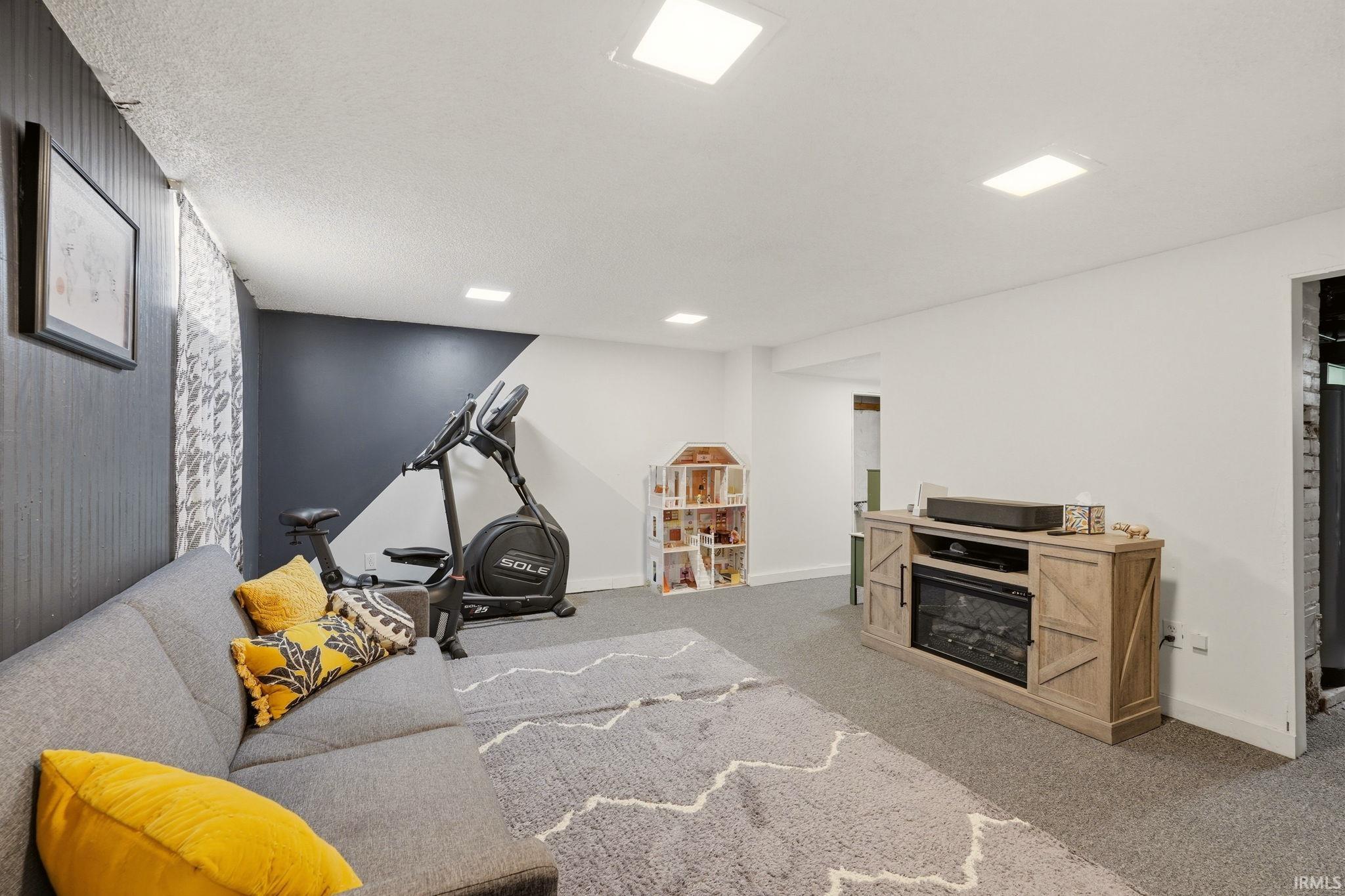 Recreational room featuring recessed lighting, a built-in electric fireplace within a wood-finish media console, dark gray accent wall paneling, and wall-to-wall carpeting